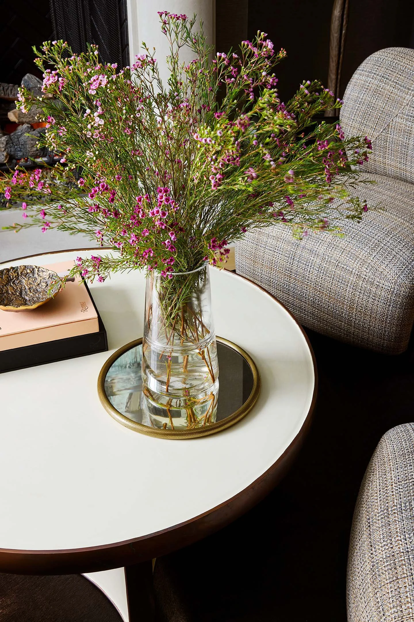 Close-up of pink floral arrangement in glass vase on round coffee table in contemporary living room.