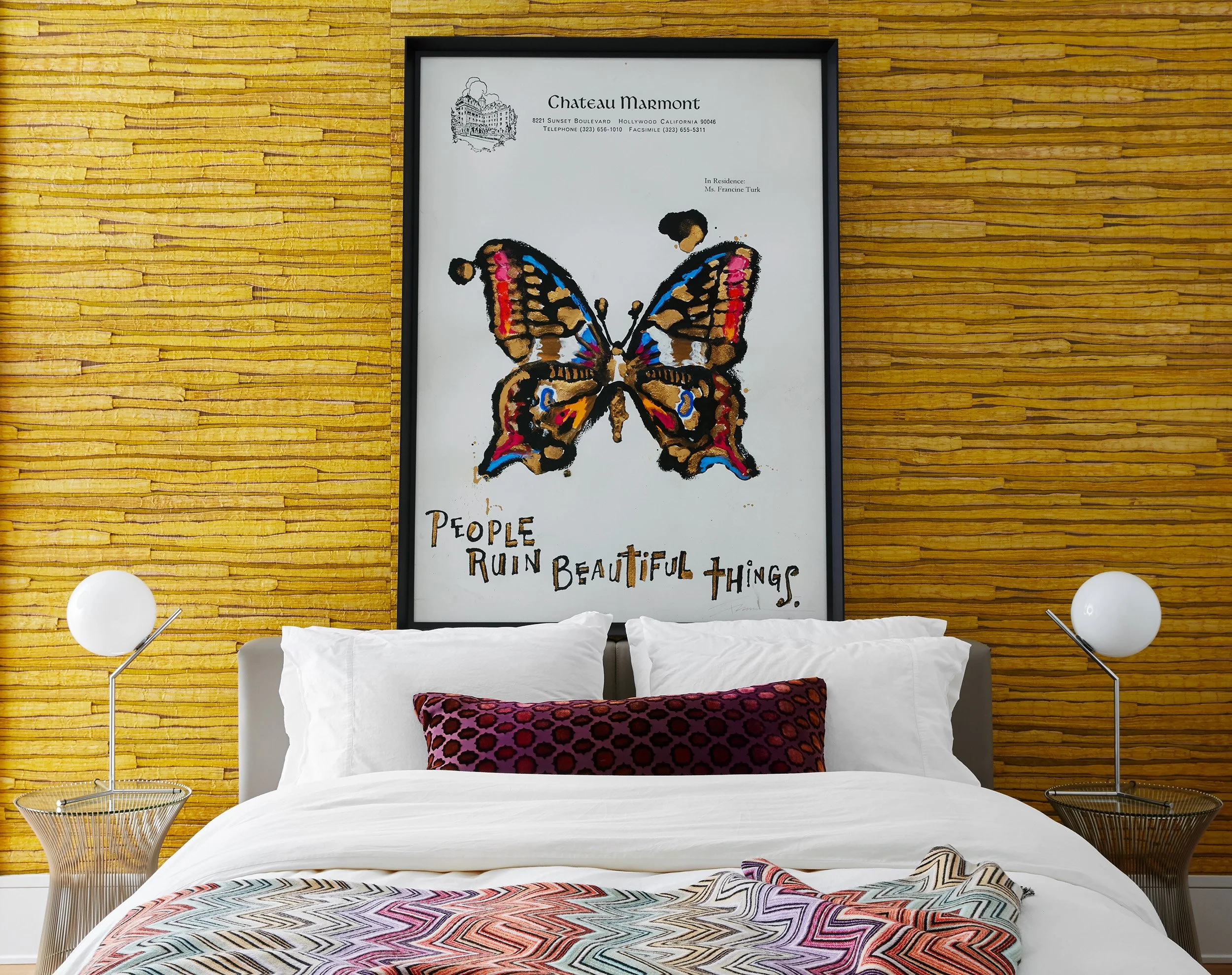 Stylish bedroom featuring a textured yellow accent wall, framed artwork above the bed, crisp white bedding, and contemporary bedside lighting.