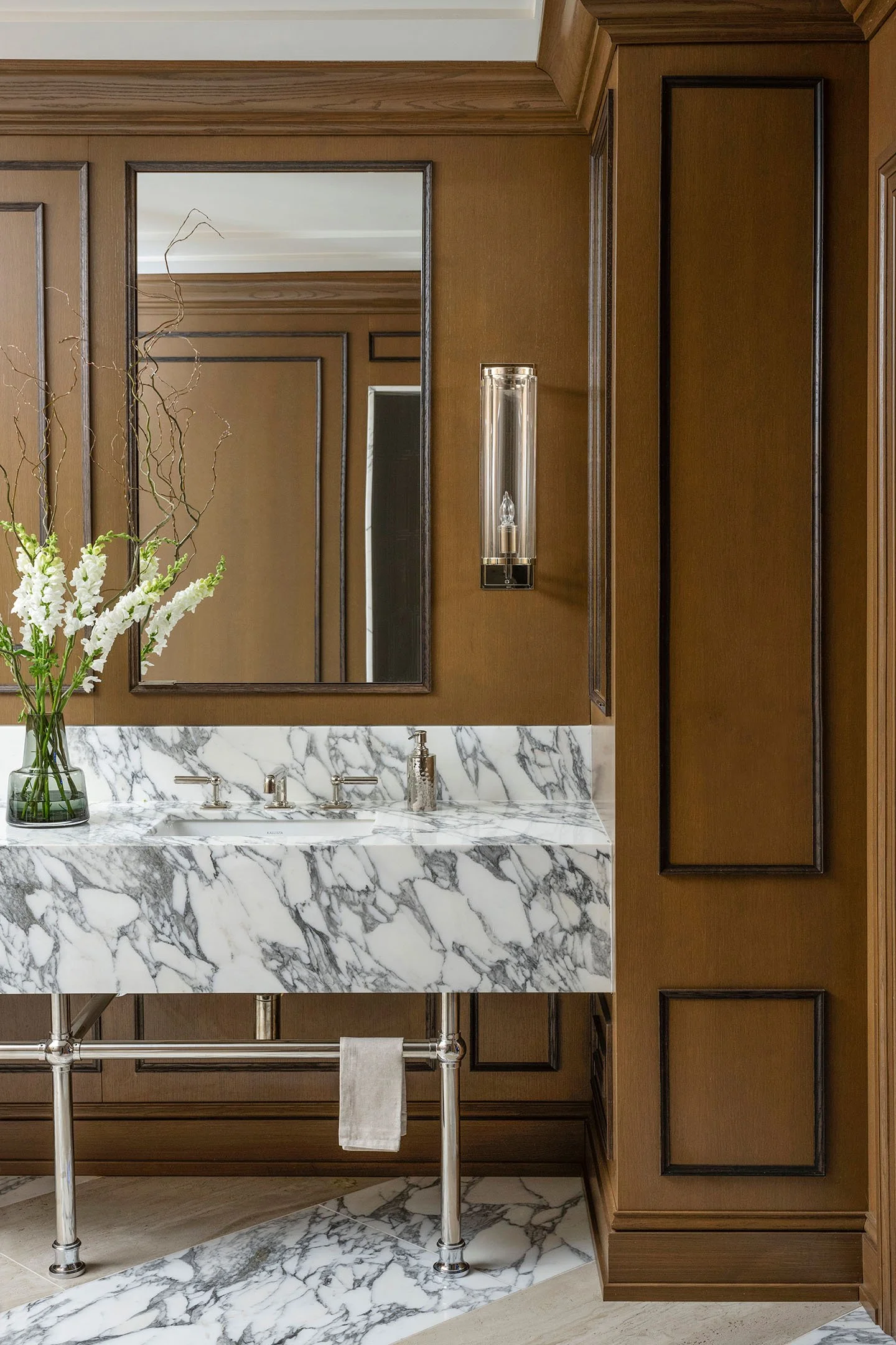 Custom marble bathroom vanity with integrated sink, polished nickel legs, wood-paneled walls, and contemporary wall sconces.