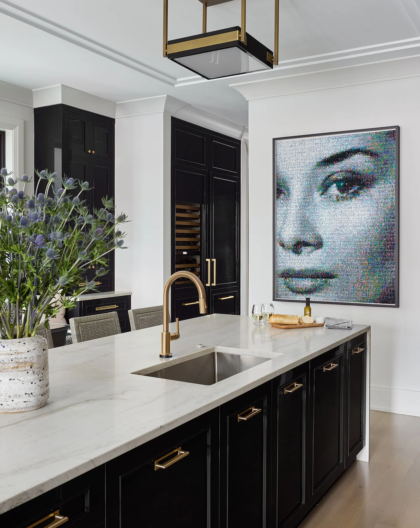 Black and white kitchen with marble island, brass hardware, custom cabinetry, and contemporary artwork.