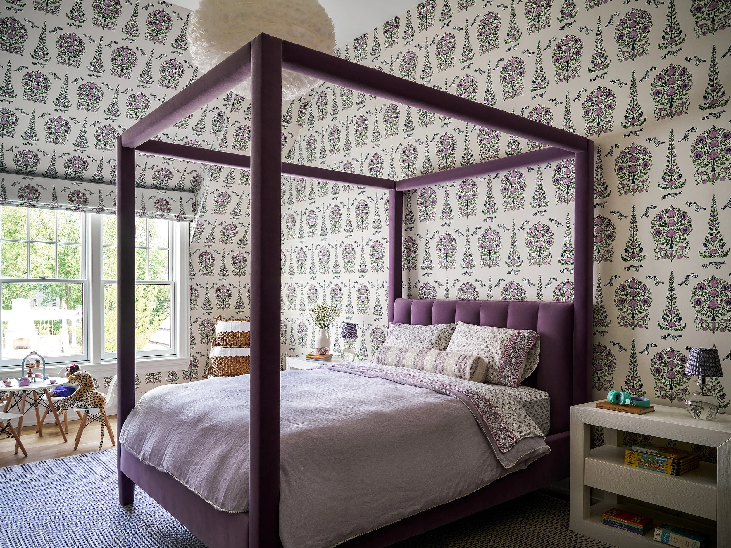 Bedroom with a purple canopy bed, patterned wallpaper, and soft coordinated textiles creating a warm atmosphere.