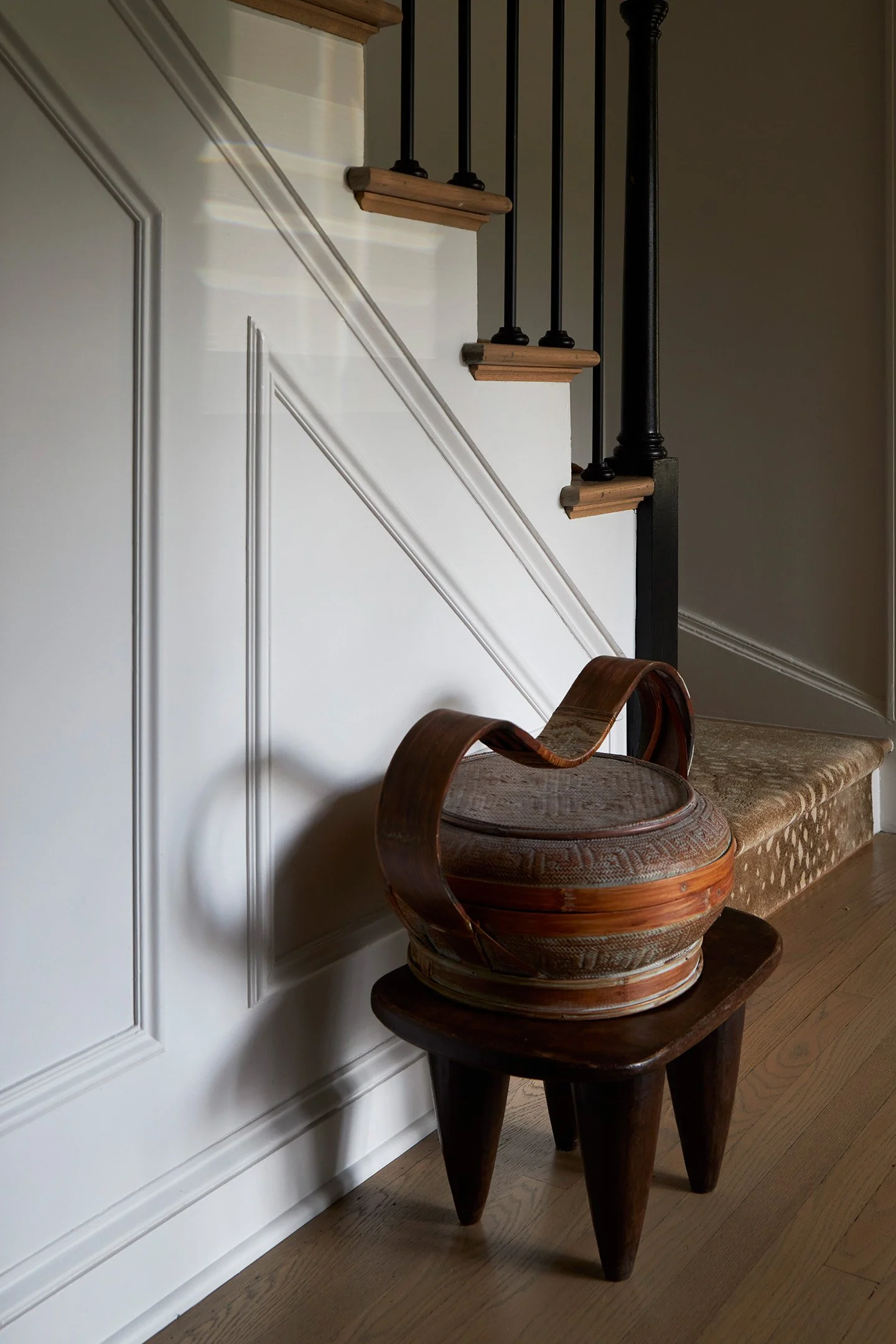 Staircase with white paneled wainscoting, wood treads, black balusters, and woven basket accent.