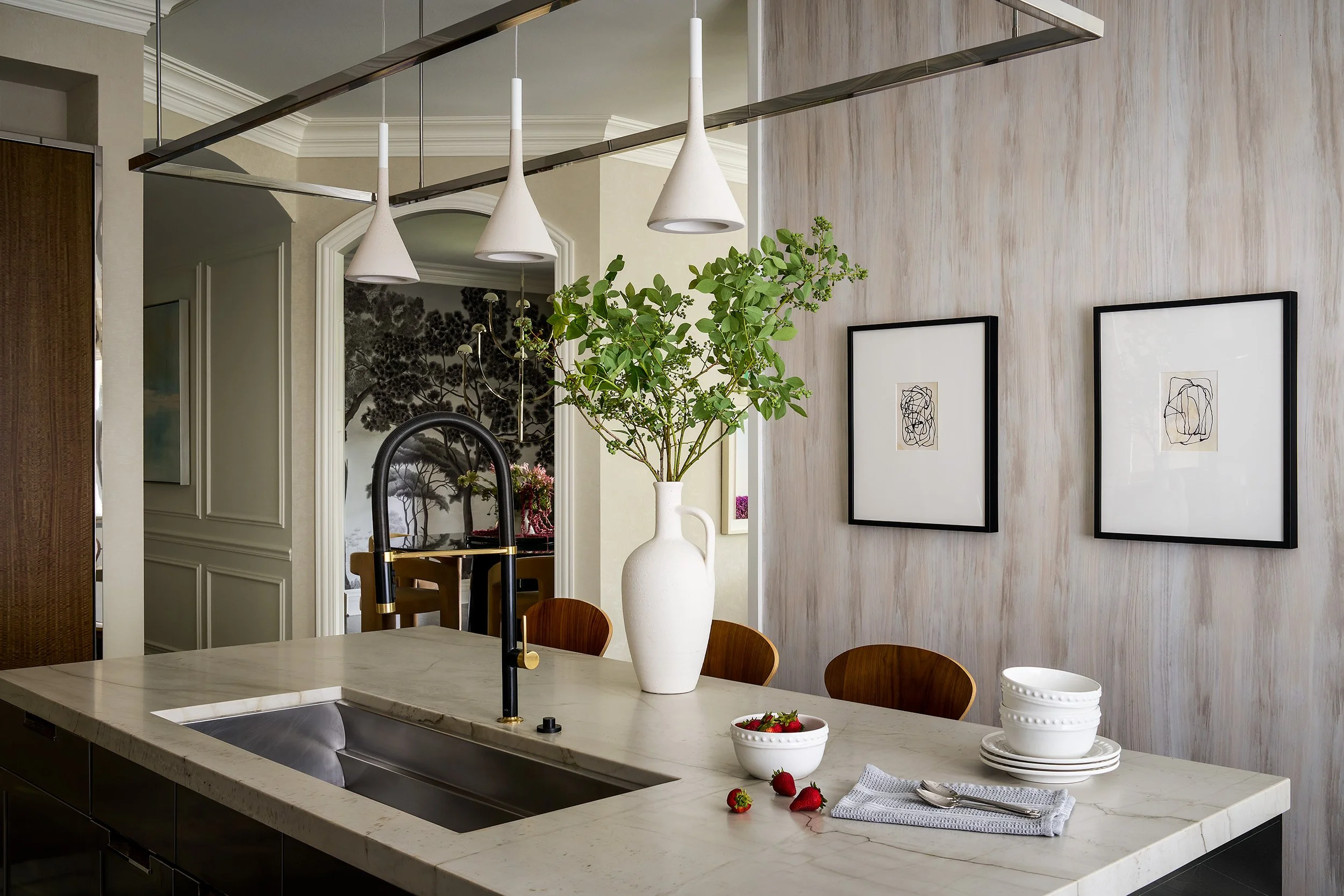 A refined kitchen featuring a marble waterfall island, sleek black faucet with brass accents, minimalist pendant lighting, and warm wood detailing.