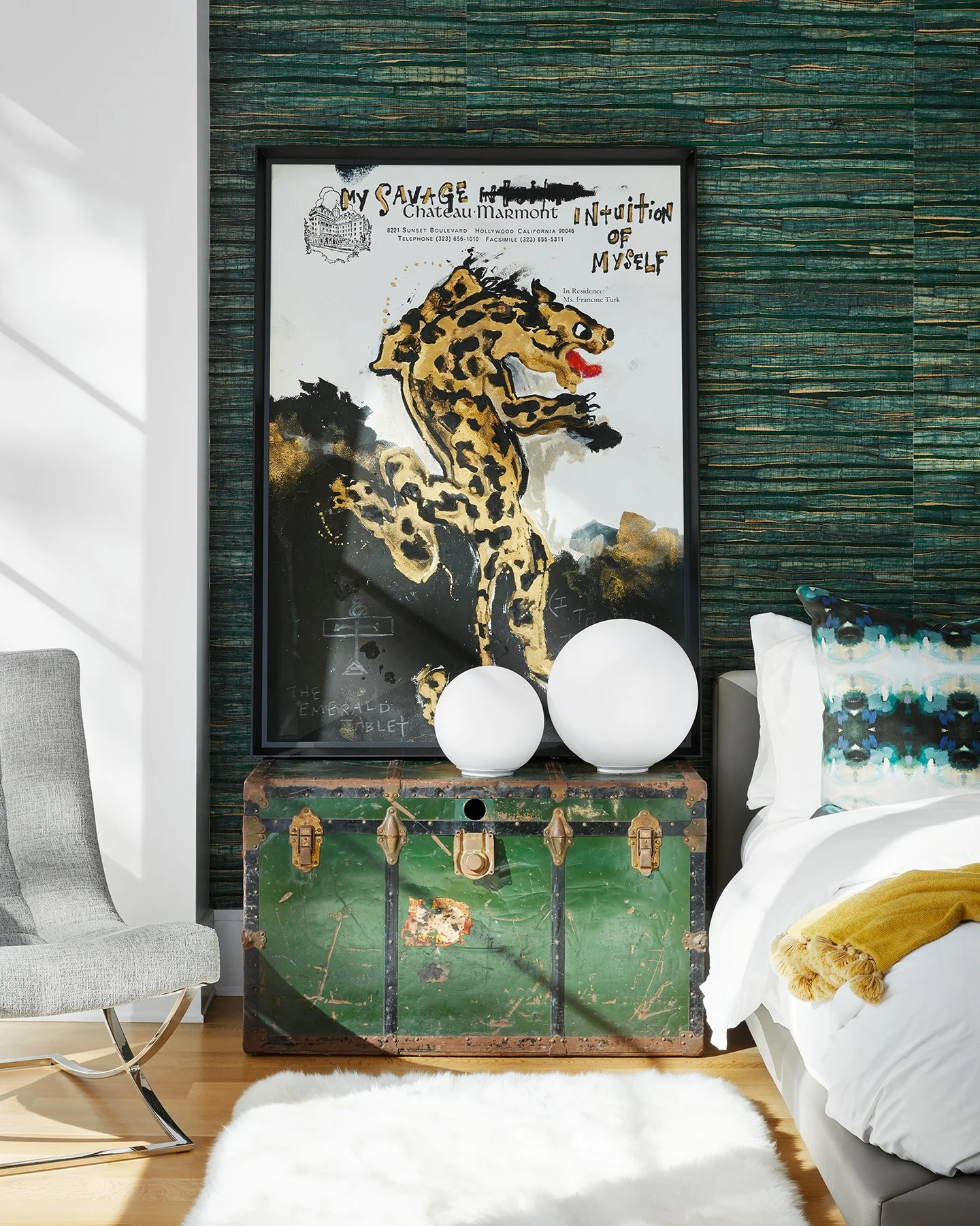 Elegant bedroom with a rich green textured feature wall, framed statement artwork, a vintage trunk nightstand, and layered bedding in neutral tones