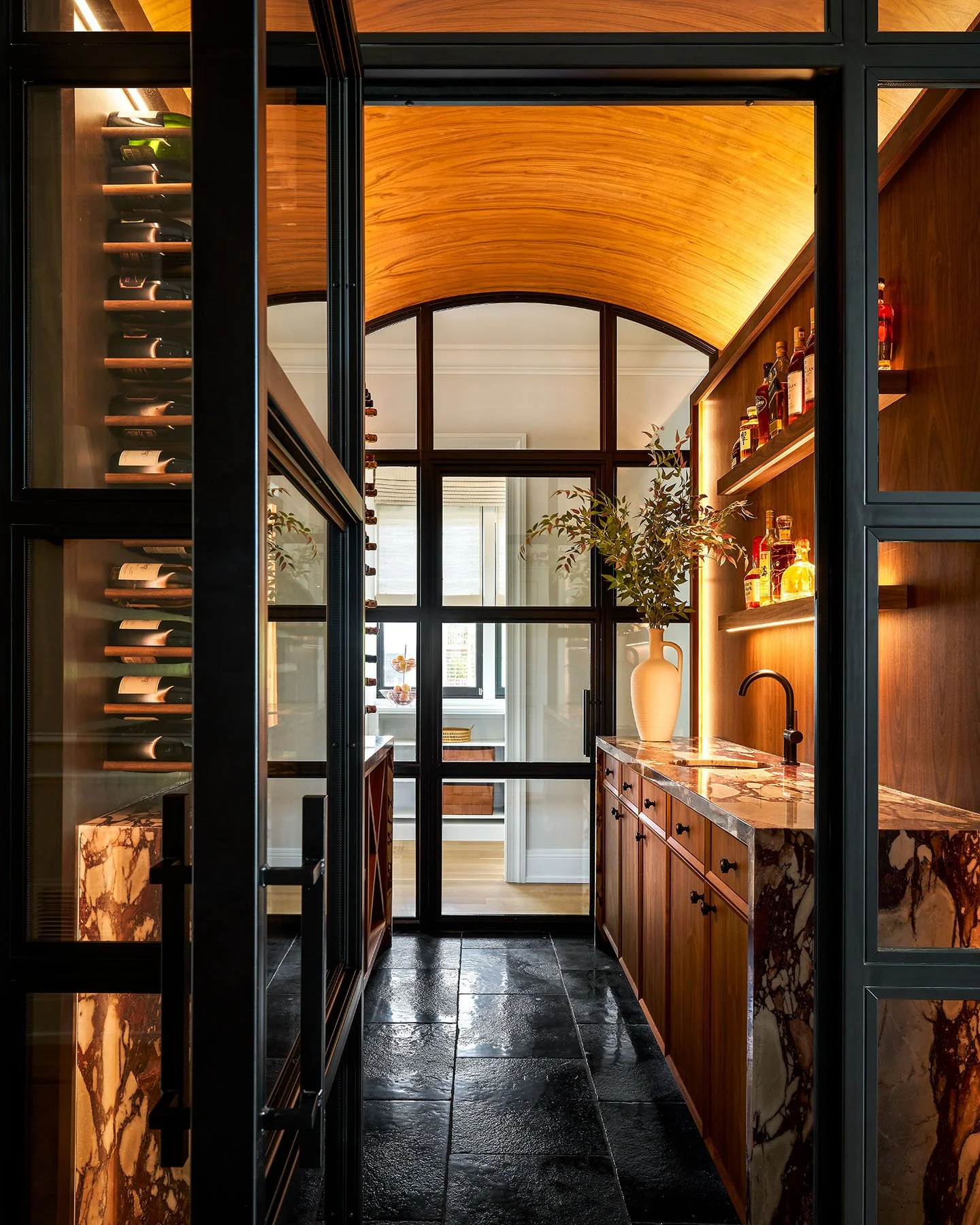 Custom wine room with glass enclosure, wood cabinetry, marble counters, and warm accent lighting.