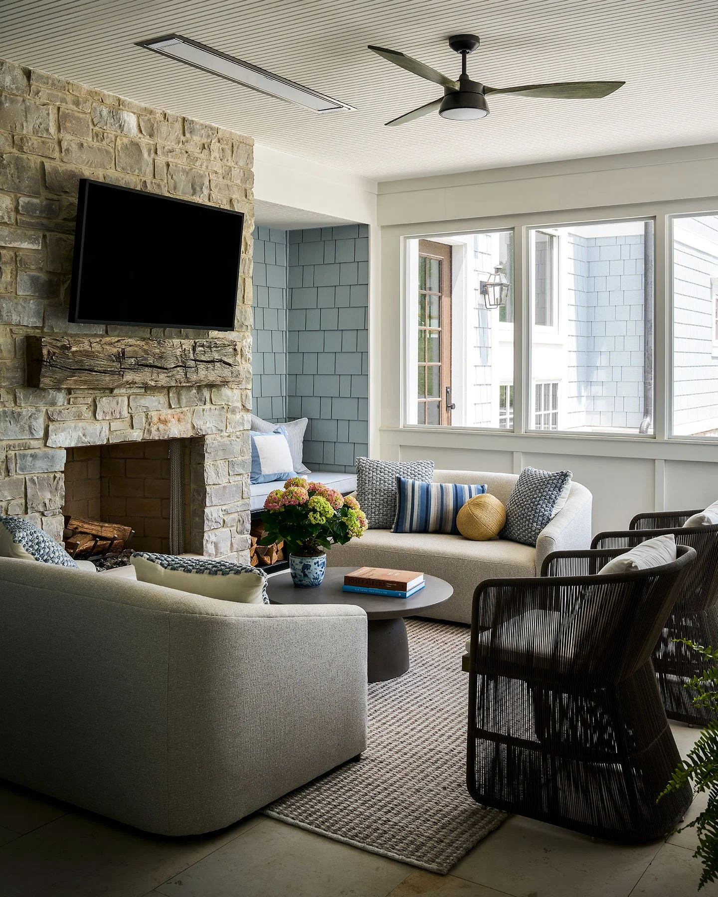 Cozy sunroom with stone fireplace, neutral seating, and woven lounge chairs in Kenilworth home.