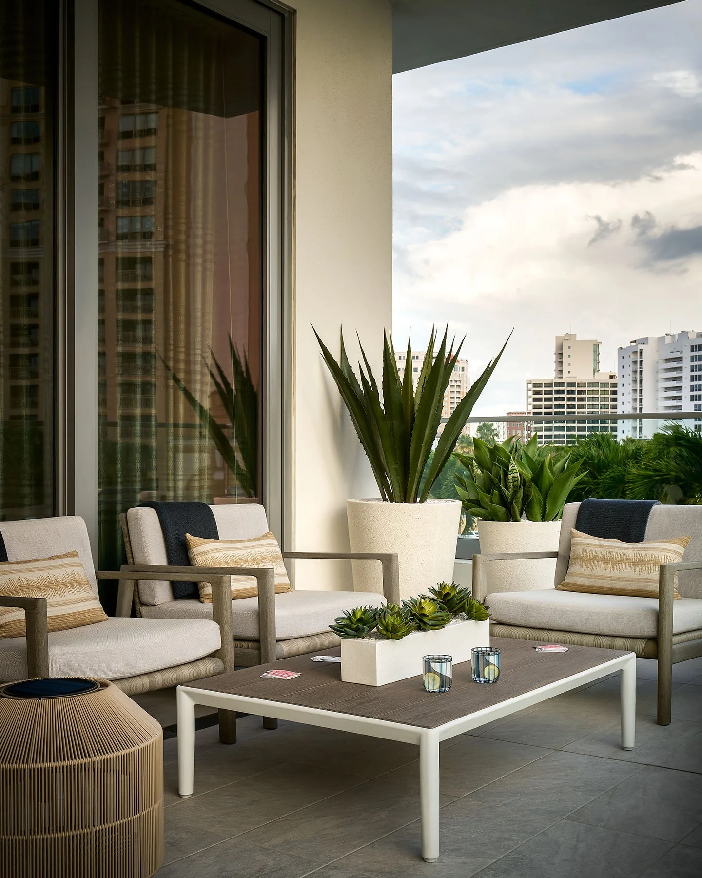 Modern balcony lounge seating with neutral armchairs, coffee table, and city waterfront views.