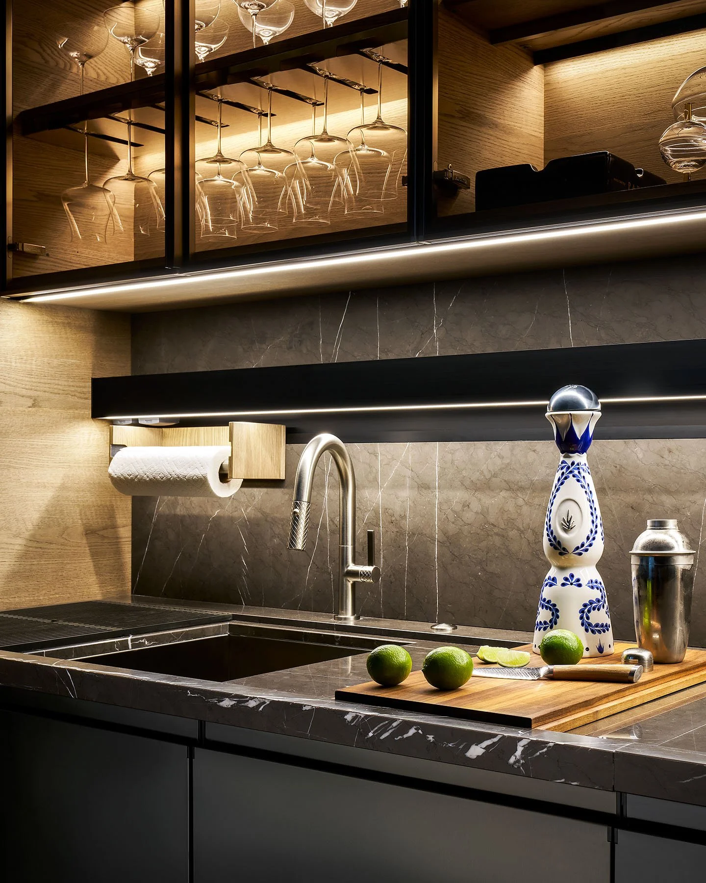 Luxury bar sink with marble backsplash, brass fixtures, and illuminated glass shelving detail.