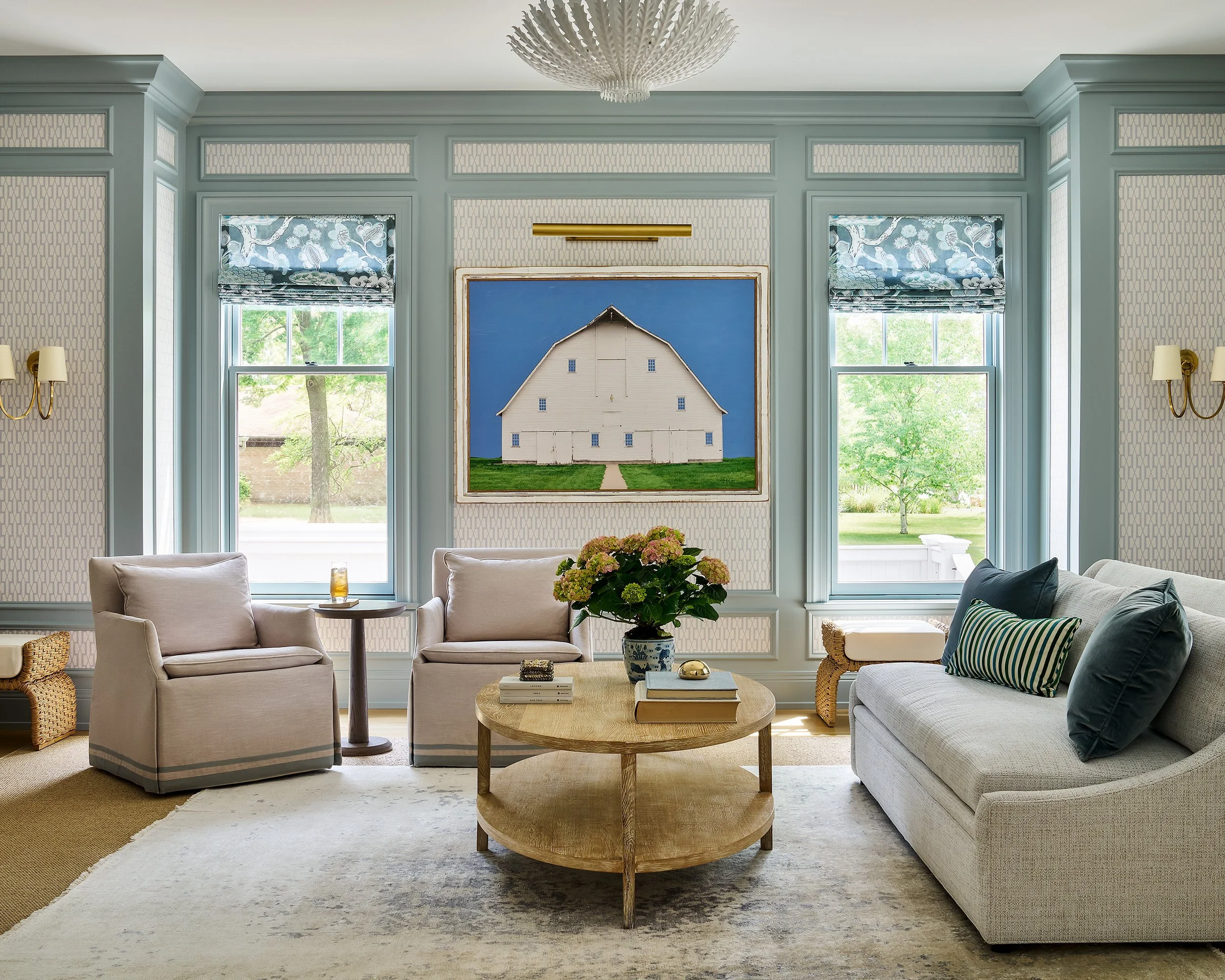 Cozy living space with soft pastel tones, symmetrical windows, and a central artwork above a round coffee table.