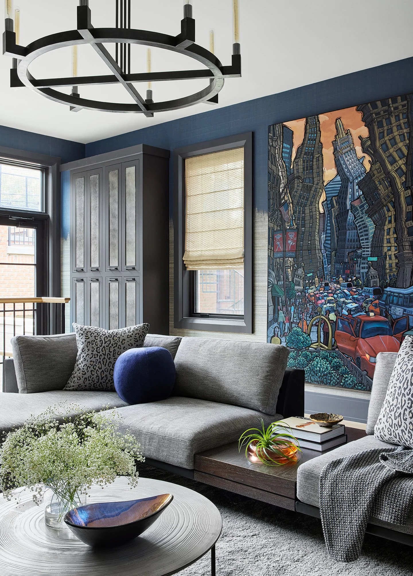 Modern blue living room with sectional sofa, large cityscape artwork, and contemporary lighting fixture.