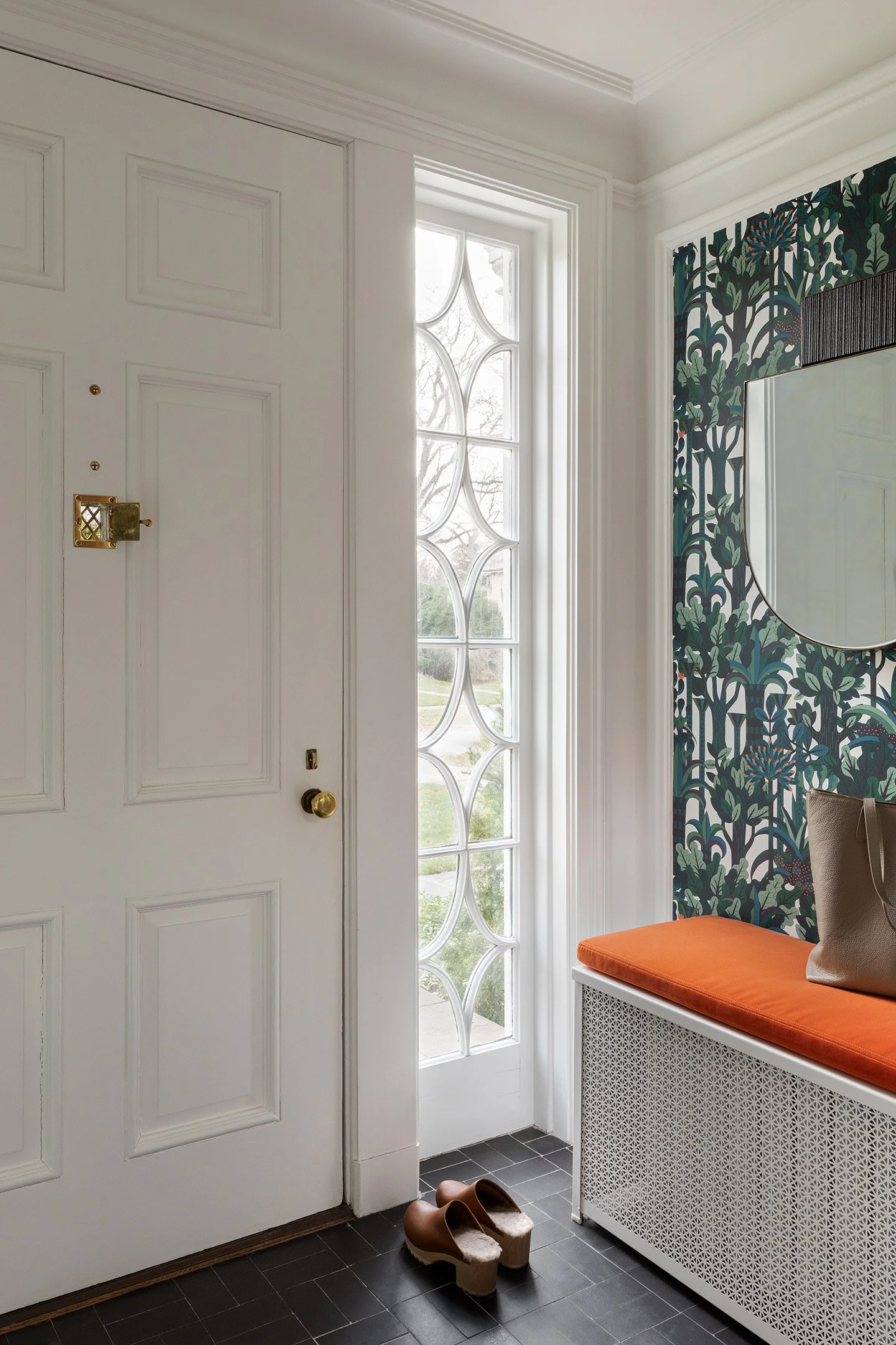 Entryway with patterned wallpaper, white built-in bench with orange cushion, and decorative glass sidelights.