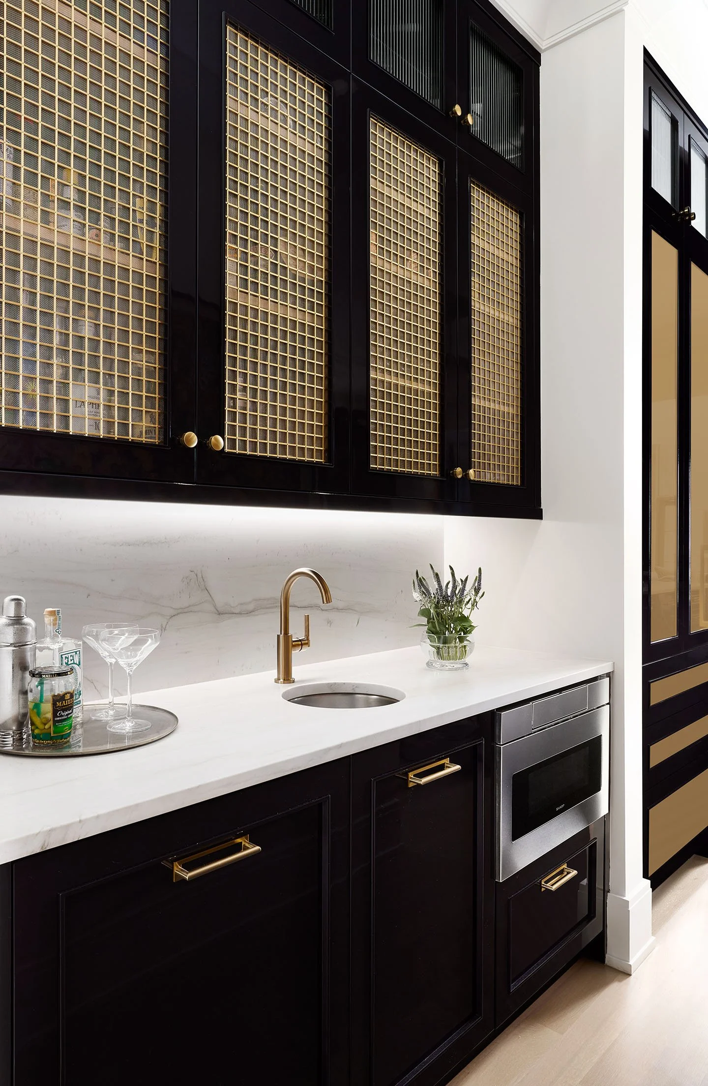 Luxury home bar with black cabinetry, brass mesh panels, marble countertop, and built-in beverage station.