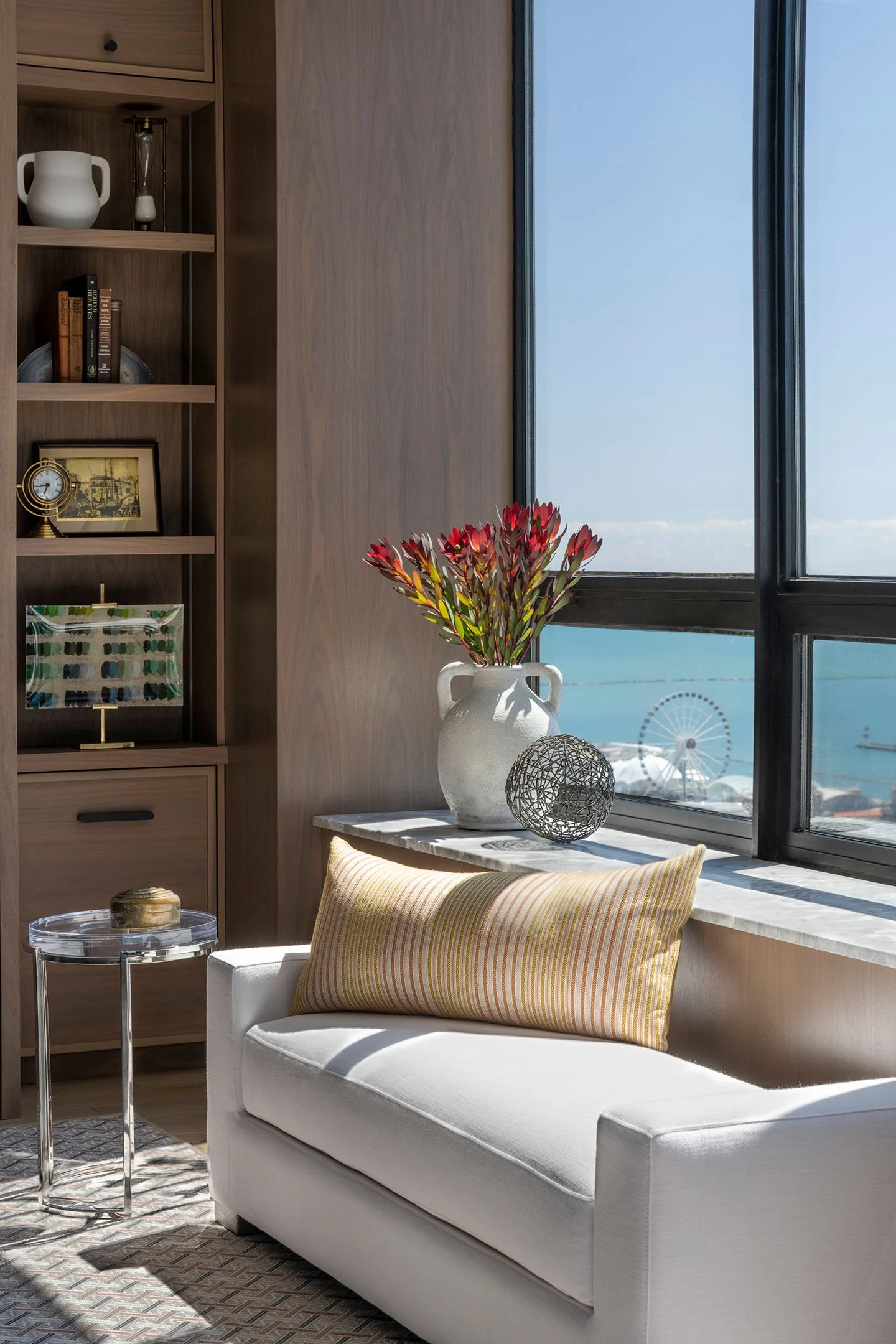 Custom built-in cabinetry with shelving, upholstered window seat, decorative styling, and waterfront views through large windows.