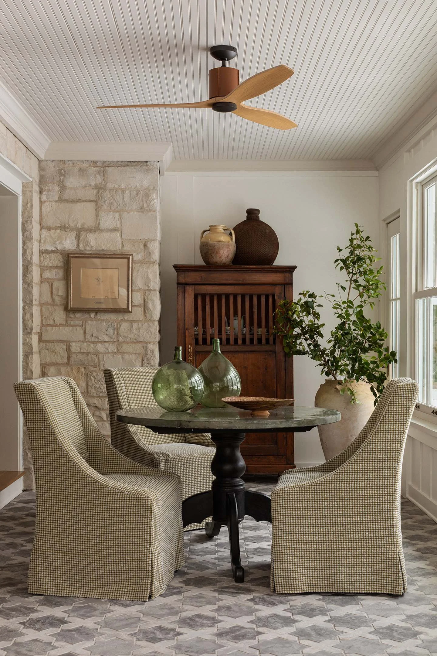 Classic breakfast nook with round pedestal table, slipcovered dining chairs, stone accent wall, and vintage wood cabinet.