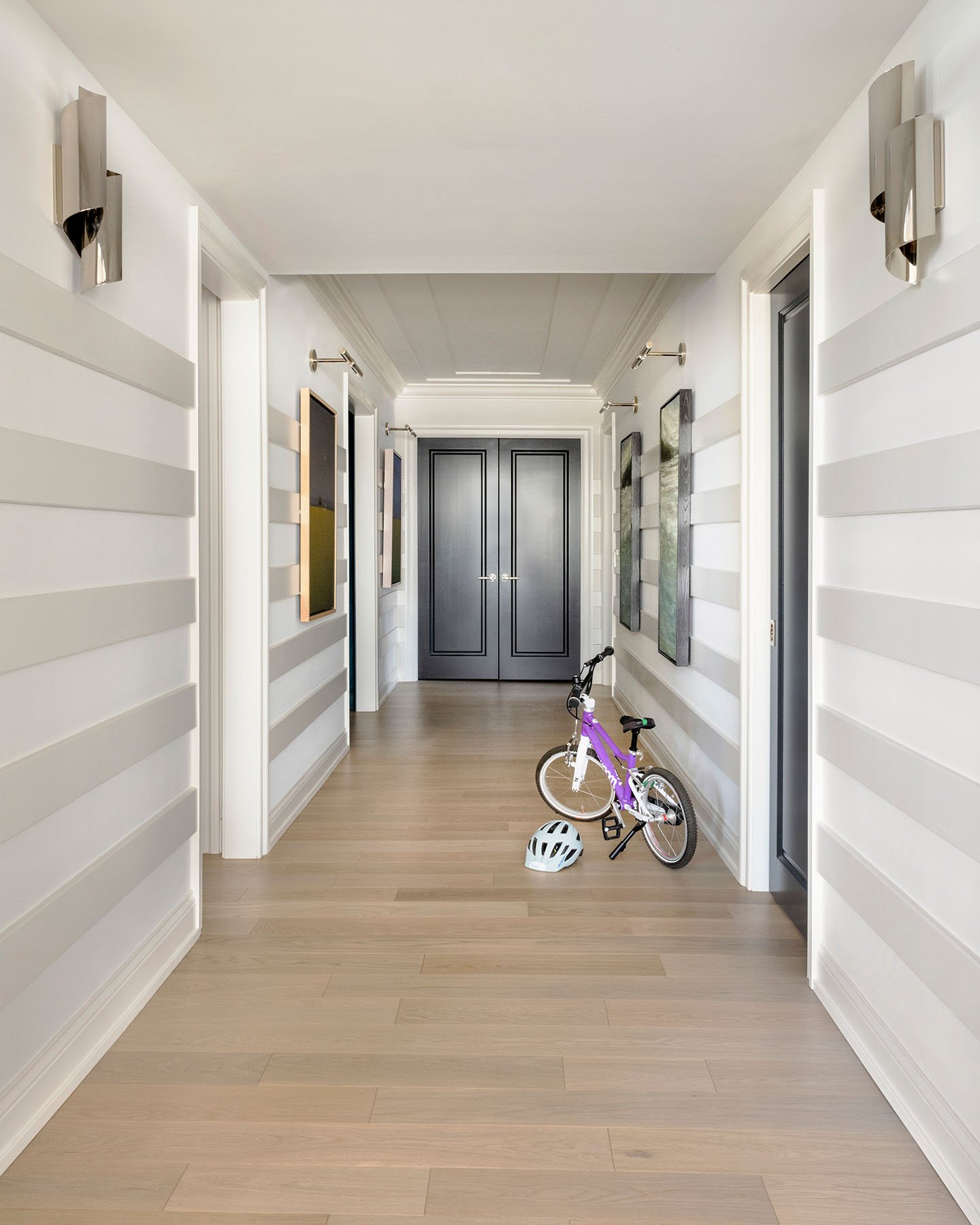 Modern hallway with horizontal striped wall detailing, light wood flooring, contemporary artwork, and custom double doors.