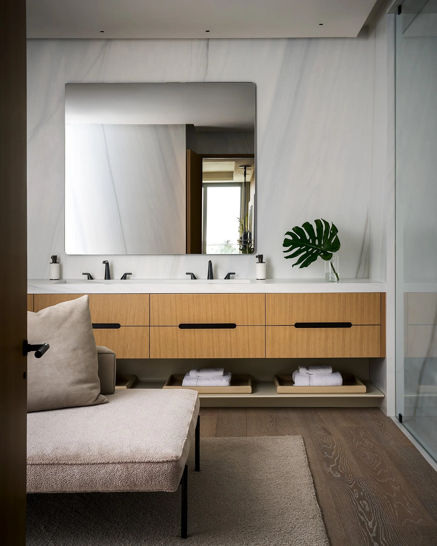 Modern bathroom with floating double vanity, wood cabinetry, black fixtures, and large marble wall backdrop.