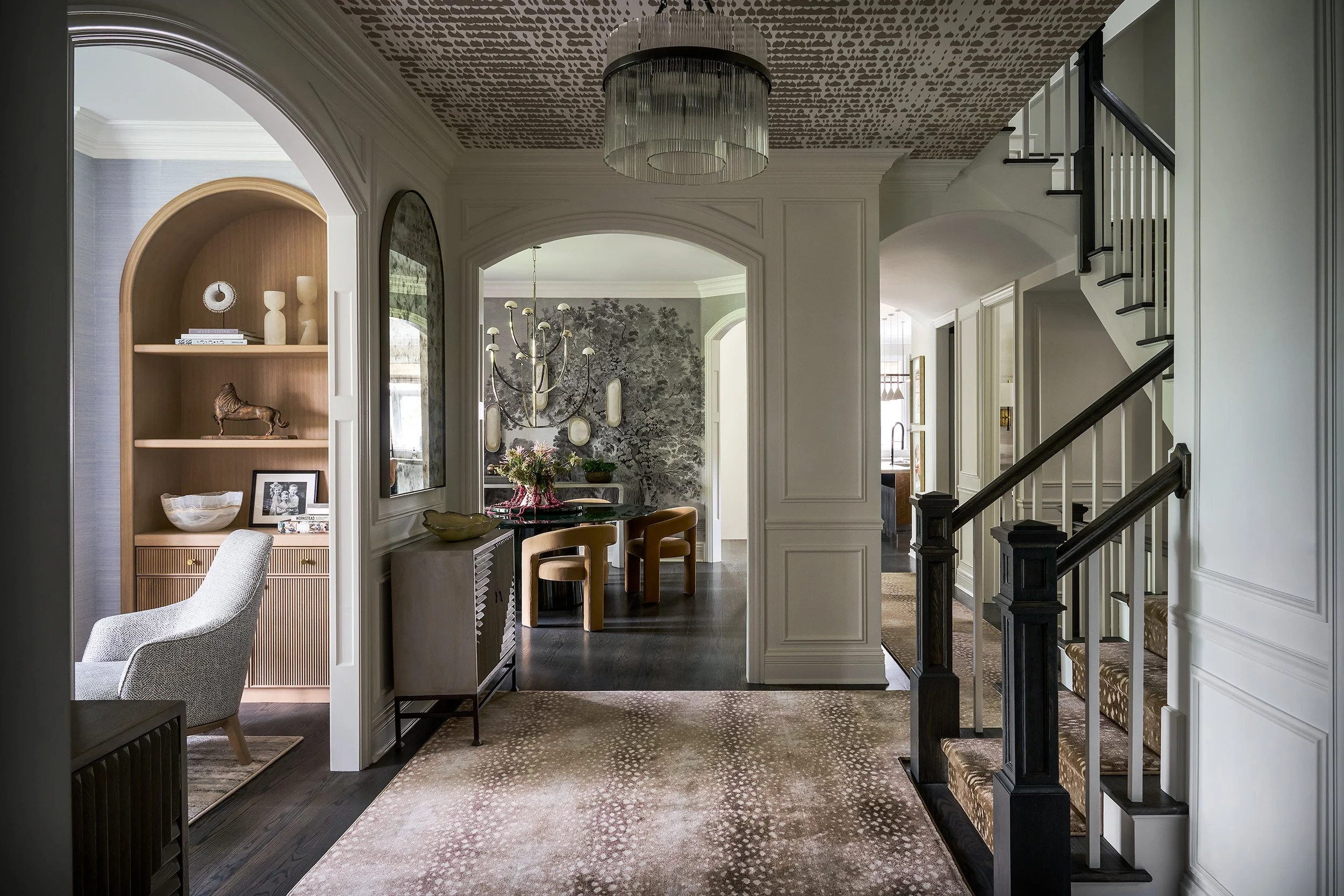 A sophisticated entry hall with architectural archways, paneled walls, and patterned ceiling detail leading into a statement dining room beyond.
