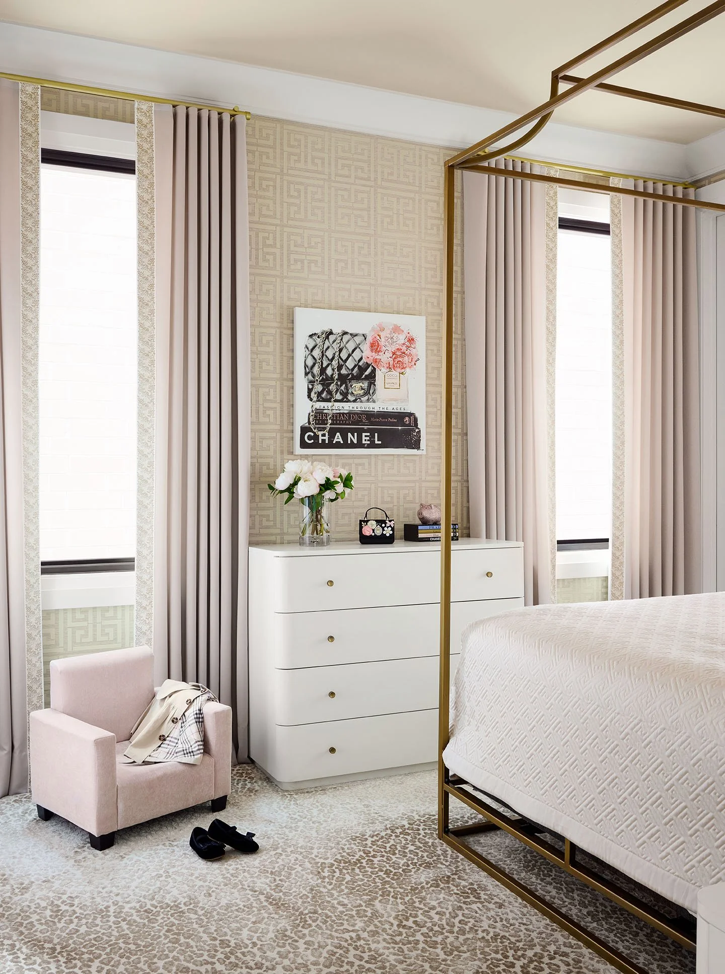 Soft feminine bedroom with gold canopy bed, blush drapery, patterned wallpaper, and white dresser styling.