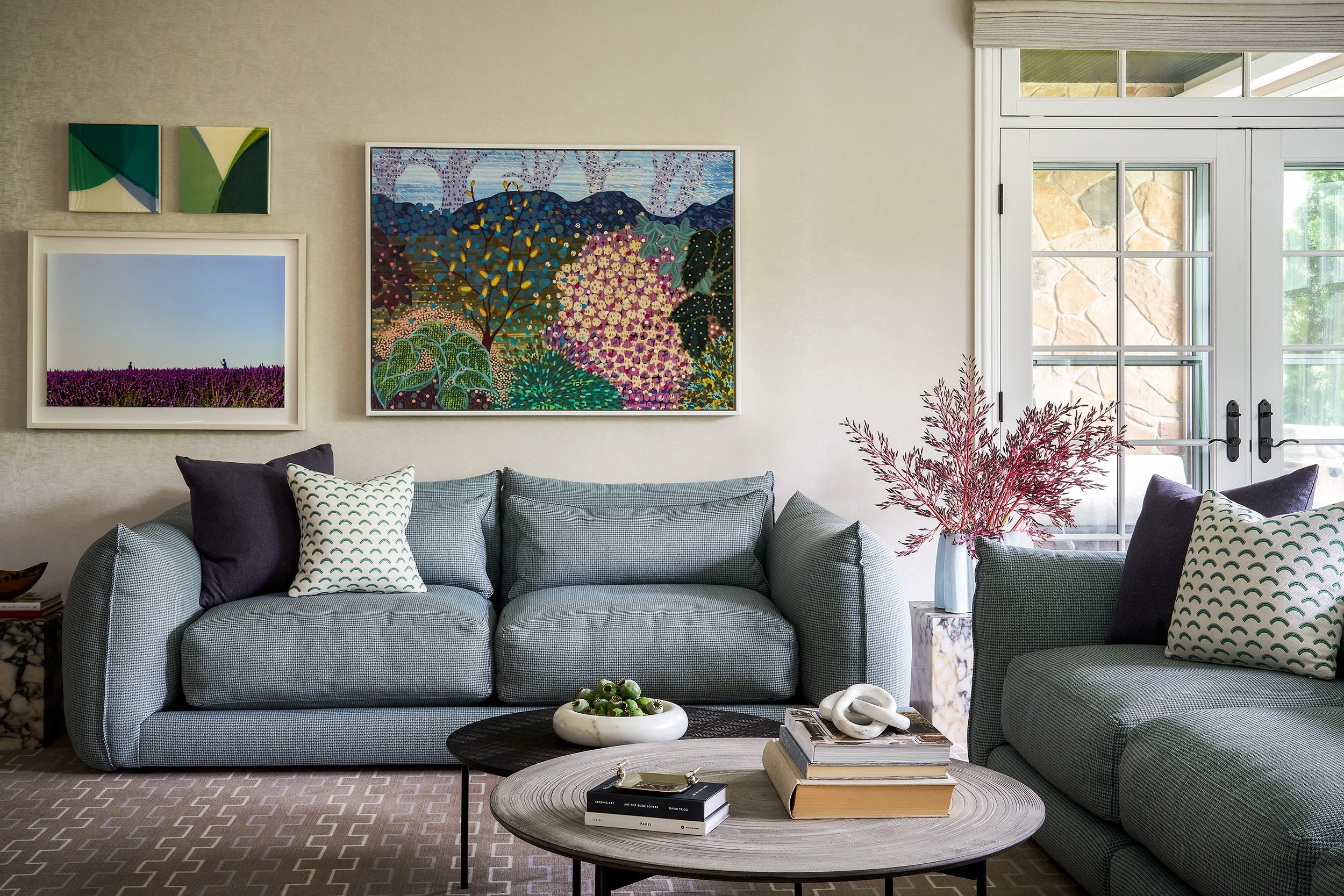 A serene sitting area featuring a soft blue sofa, layered modern artwork, textured rug, and marble side tables styled with sculptural accents.