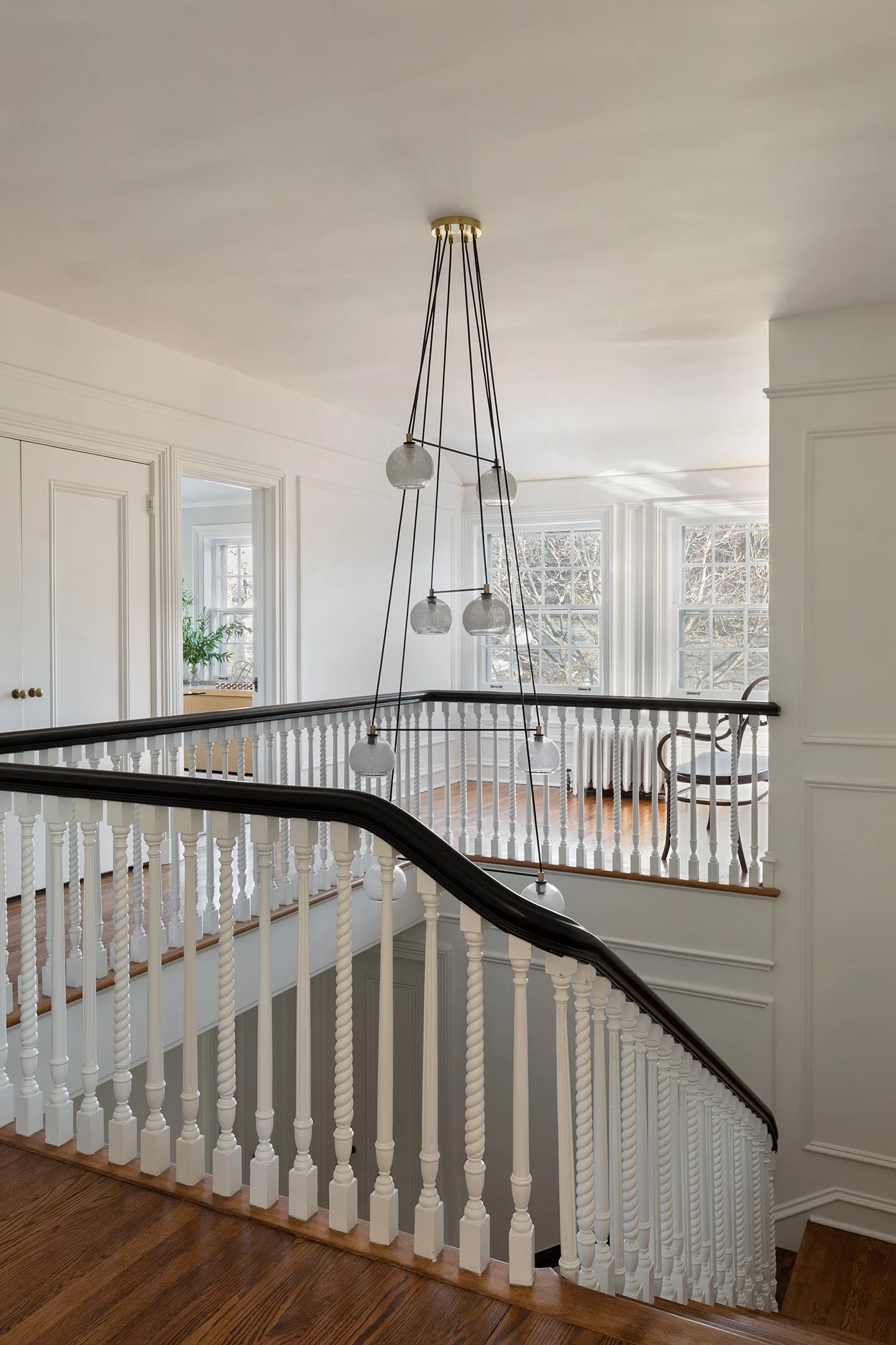 Curved staircase with white balusters, dark wood railing, and multi-globe pendant chandelier.