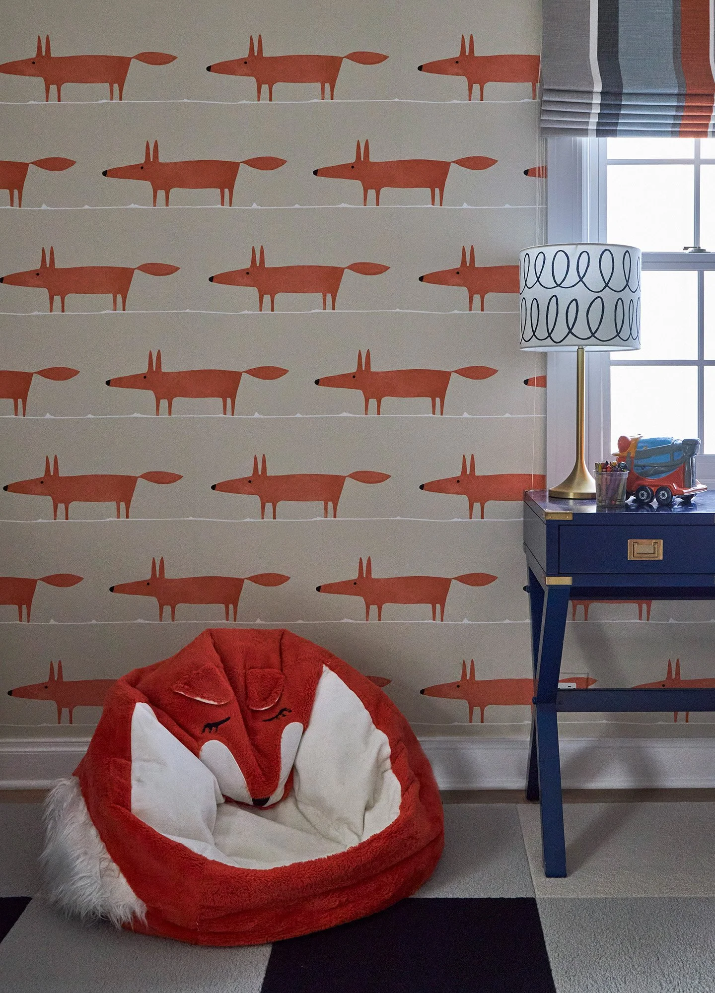 Children’s room with fox patterned wallpaper, plush fox chair, and navy side table with lamp.