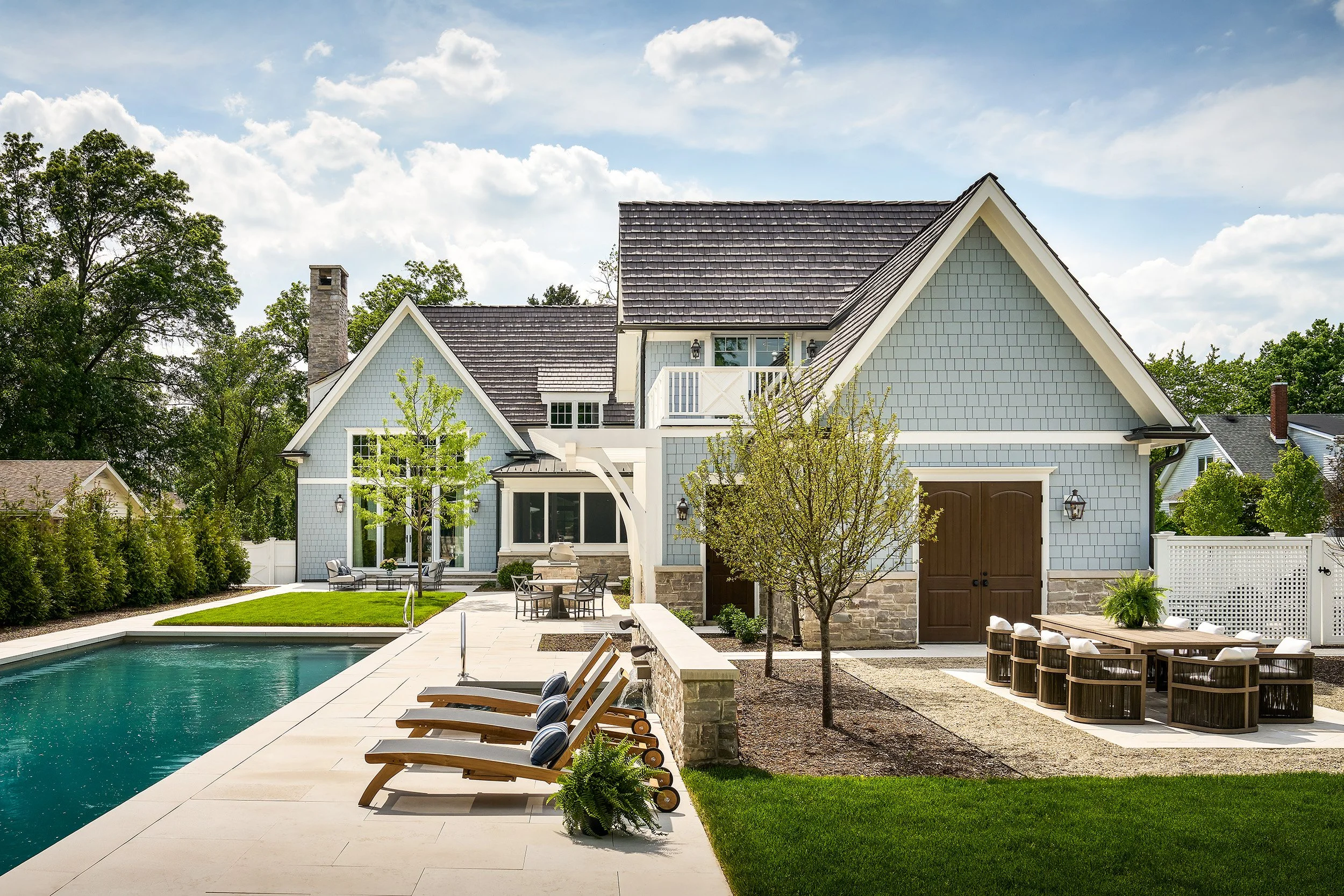 Elegant exterior of a modern coastal-style home with a backyard pool, lounge seating, and landscaped garden.