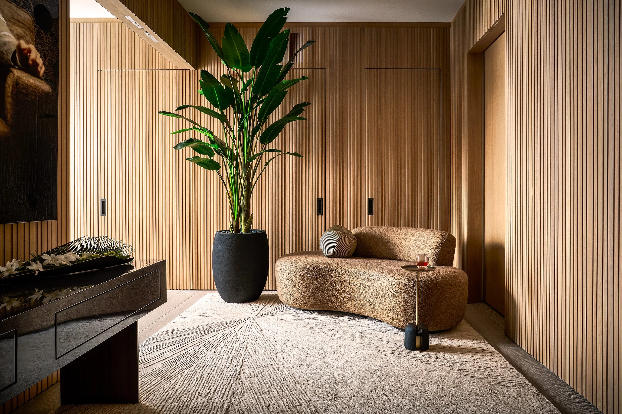 Contemporary lounge area with curved sofa, indoor plant, and textured wood panel walls