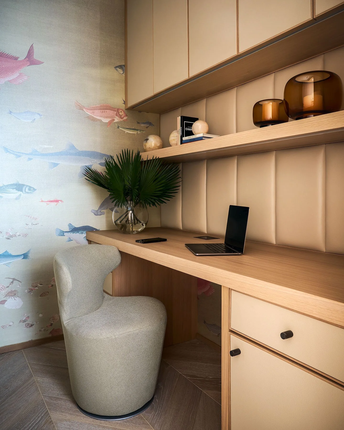 Custom built-in desk with wood cabinetry, upholstered wall panels, floating shelves, and integrated workspace lighting.
