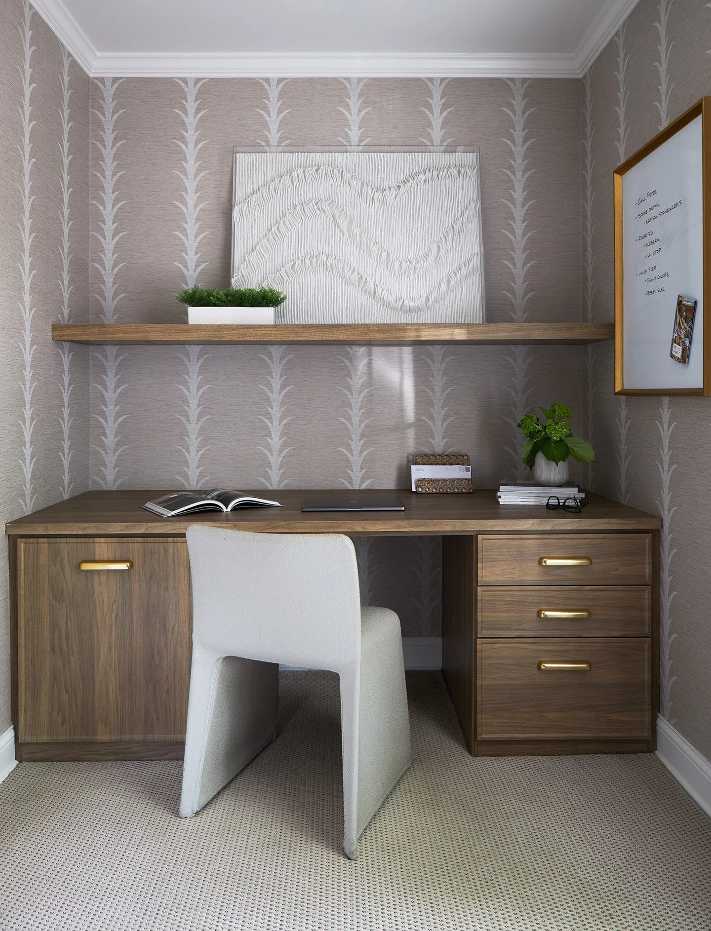 Compact home office with walnut built-in desk, brass hardware, floating shelf, and textured wallpaper.