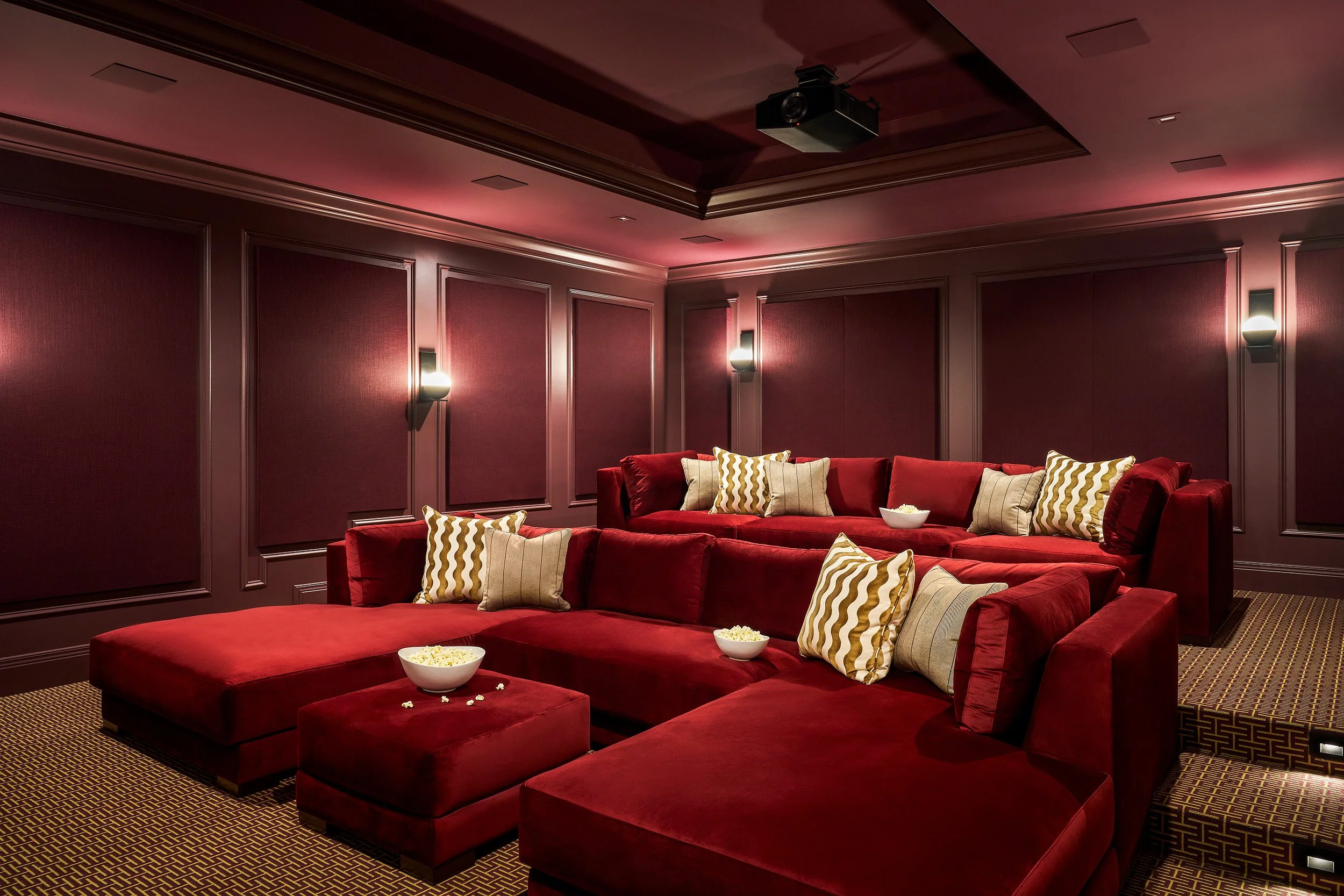 Home theater room with plush red sectional seating, paneled walls, and ambient lighting for a cinematic experience.