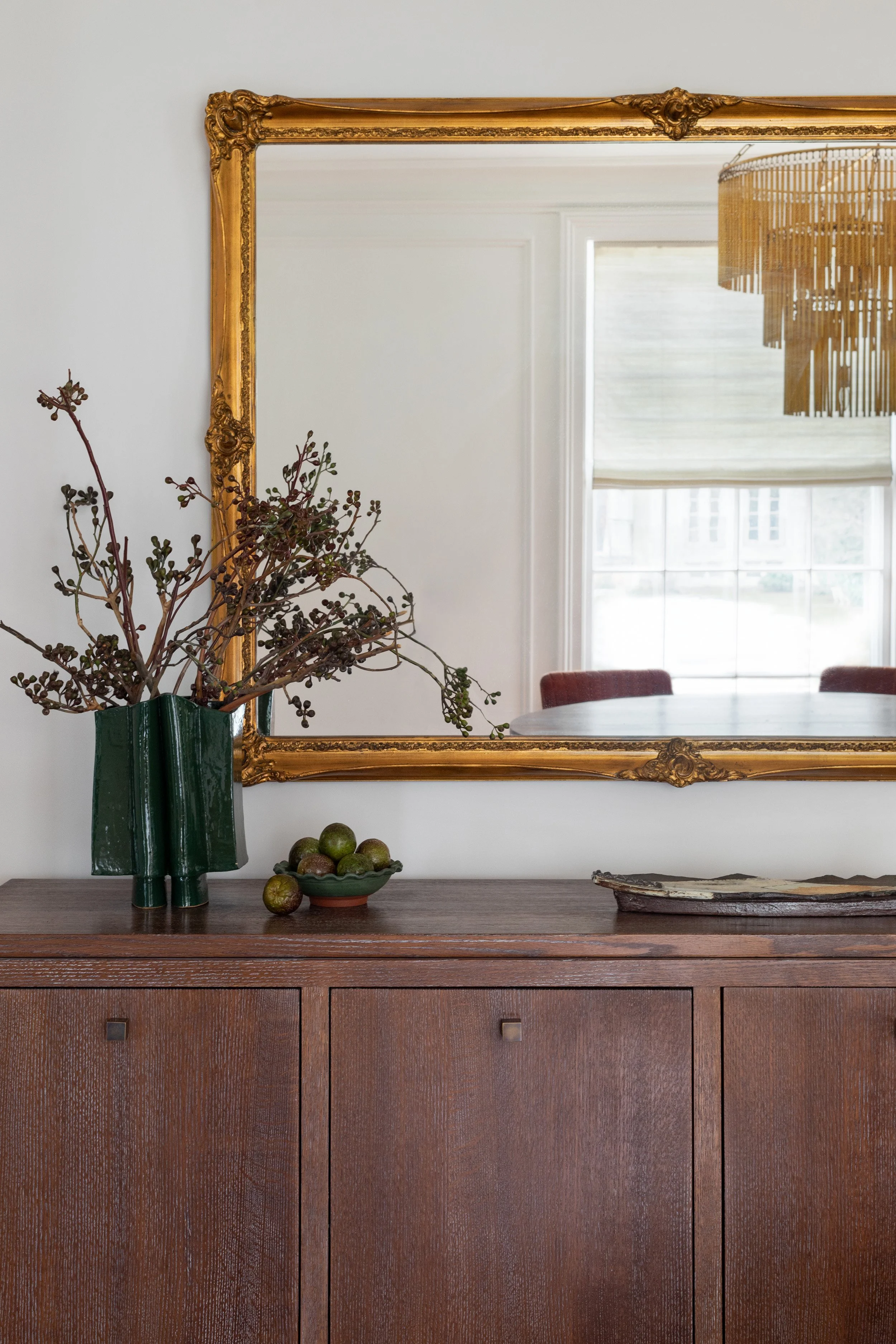 Wood sideboard styled with green ceramic vase, decorative bowl, and ornate gold mirror above.