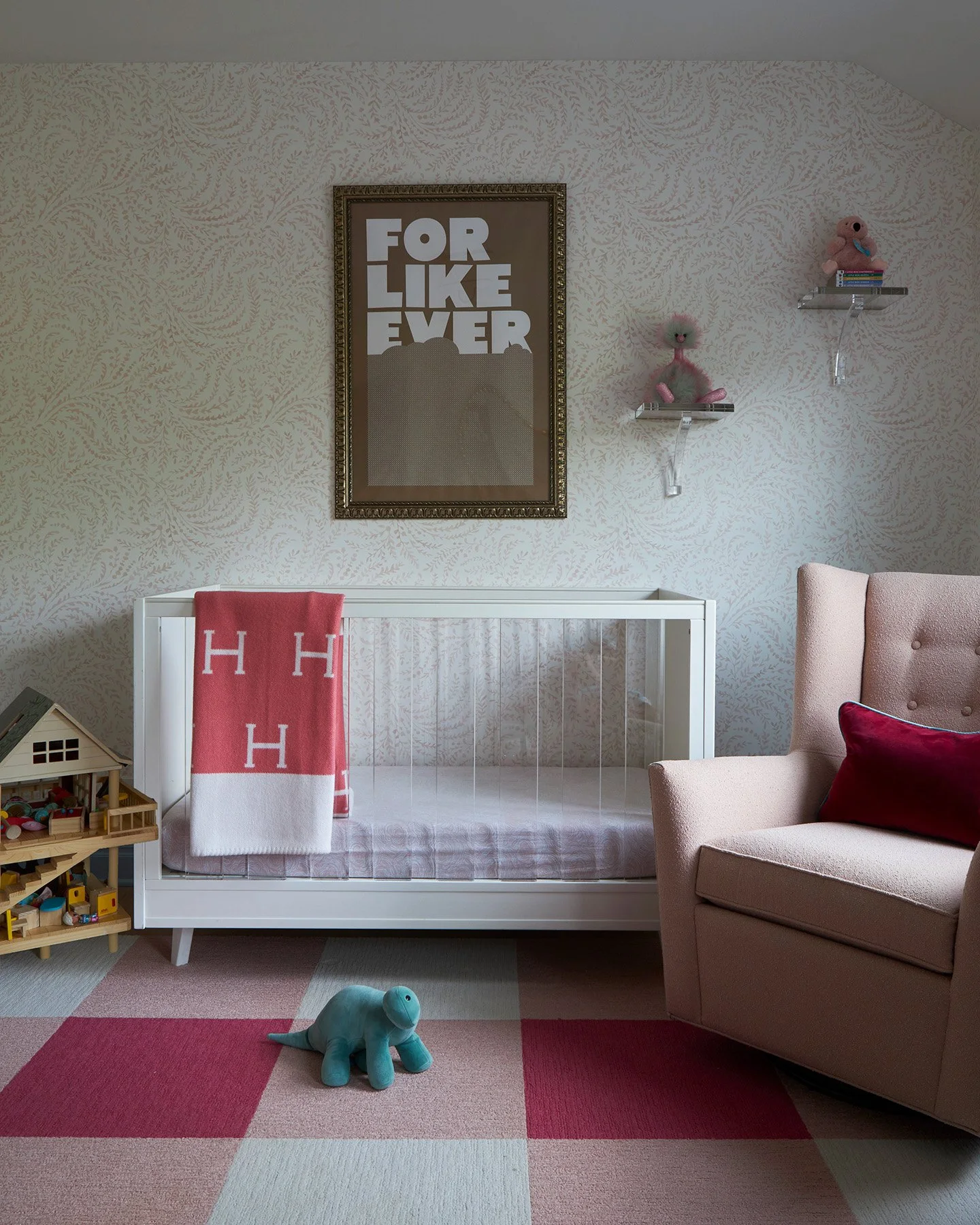 Soft pink nursery with white crib, framed art, upholstered glider, and pink checkered area rug.