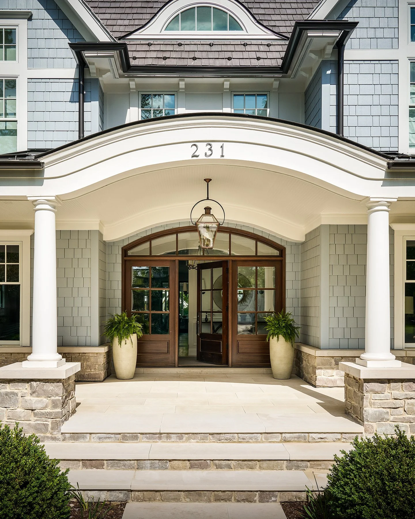 Front entry of custom shingle-style home with arched portico, stone steps, and double wood doors in Kenilworth, Illinois.