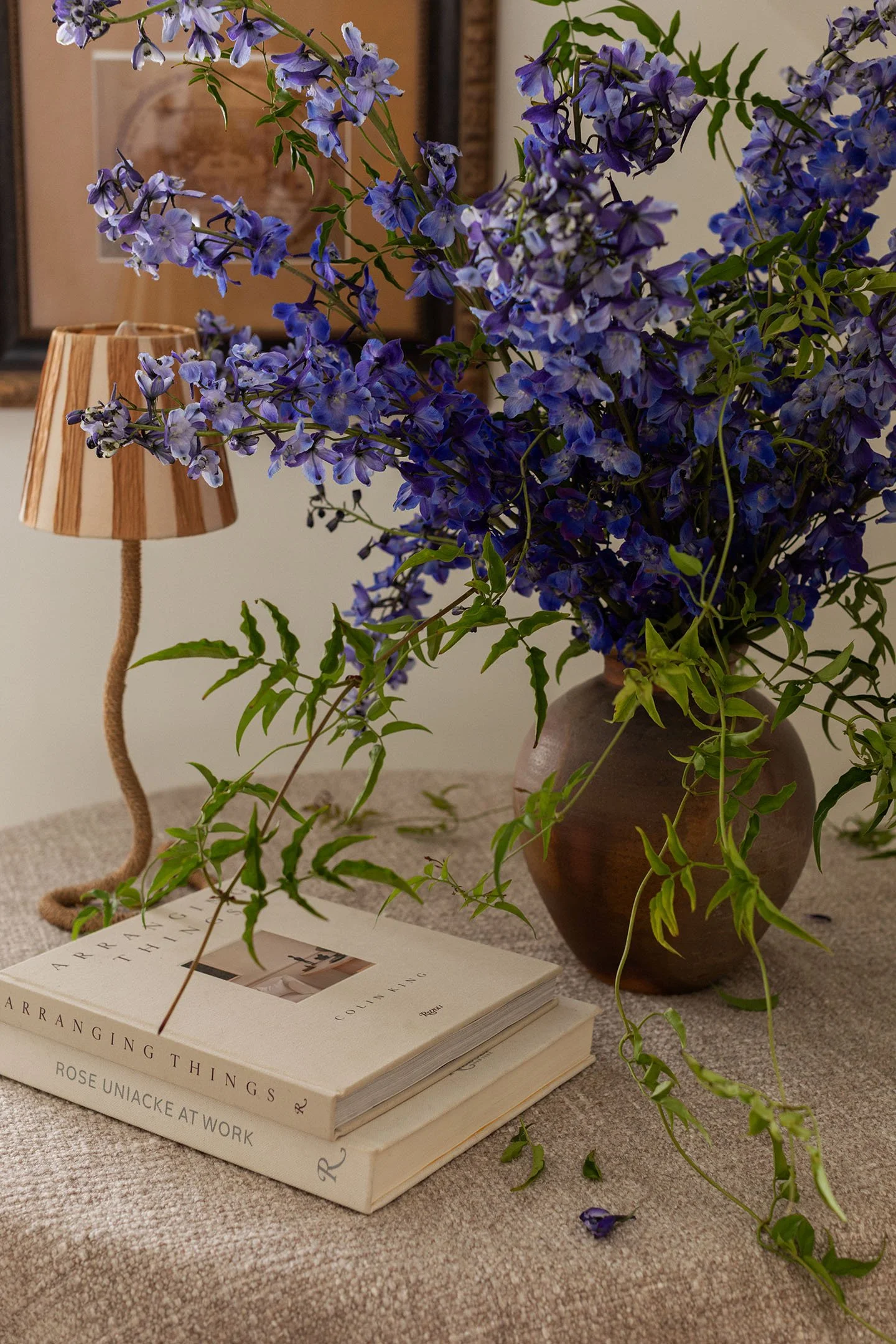 Blue floral arrangement in rustic vase styled on draped entry table with decorative books and accent lamp.