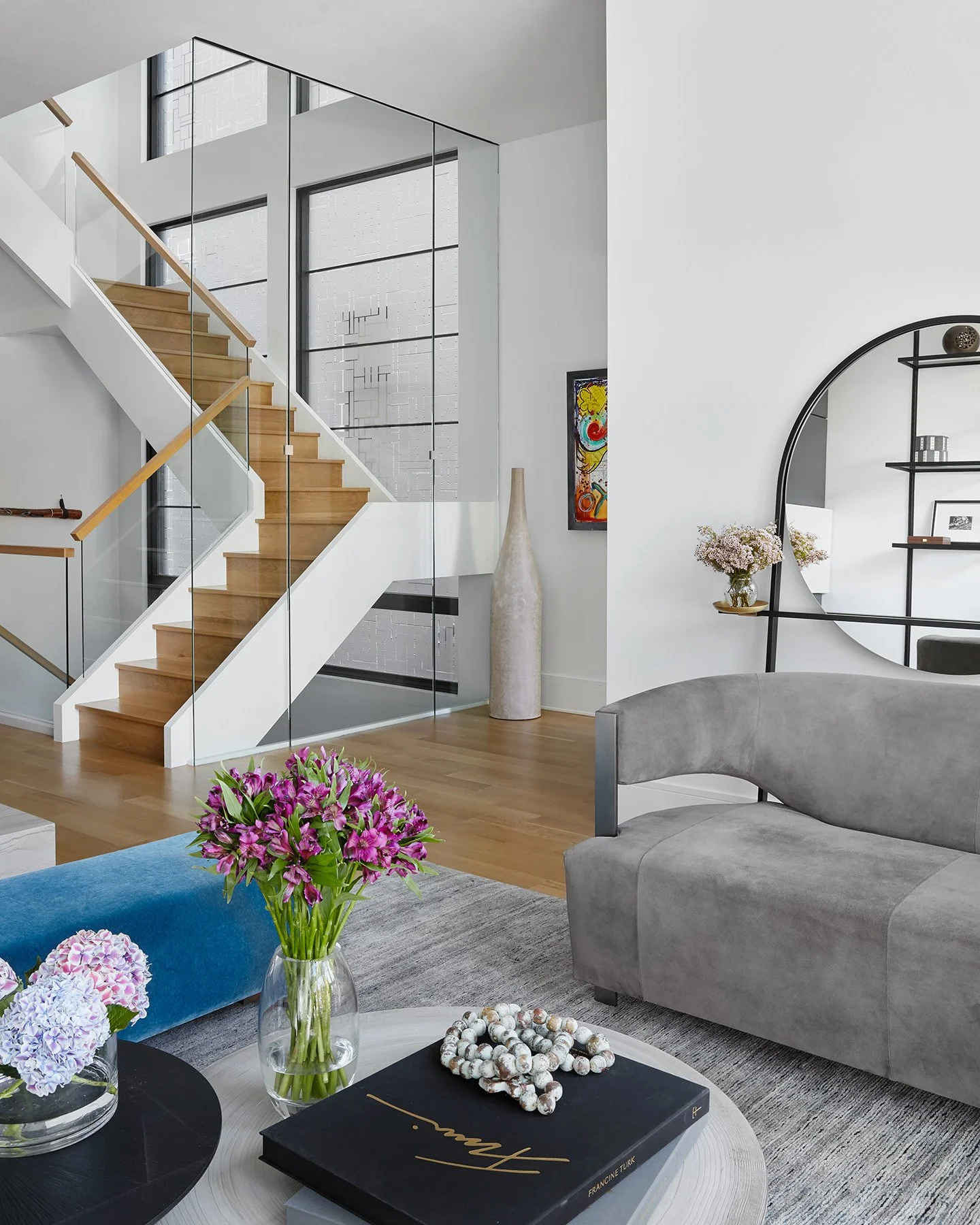 Light-filled open living space with a floating wood staircase and glass railing, soft neutral furnishings, and contemporary decor accents.