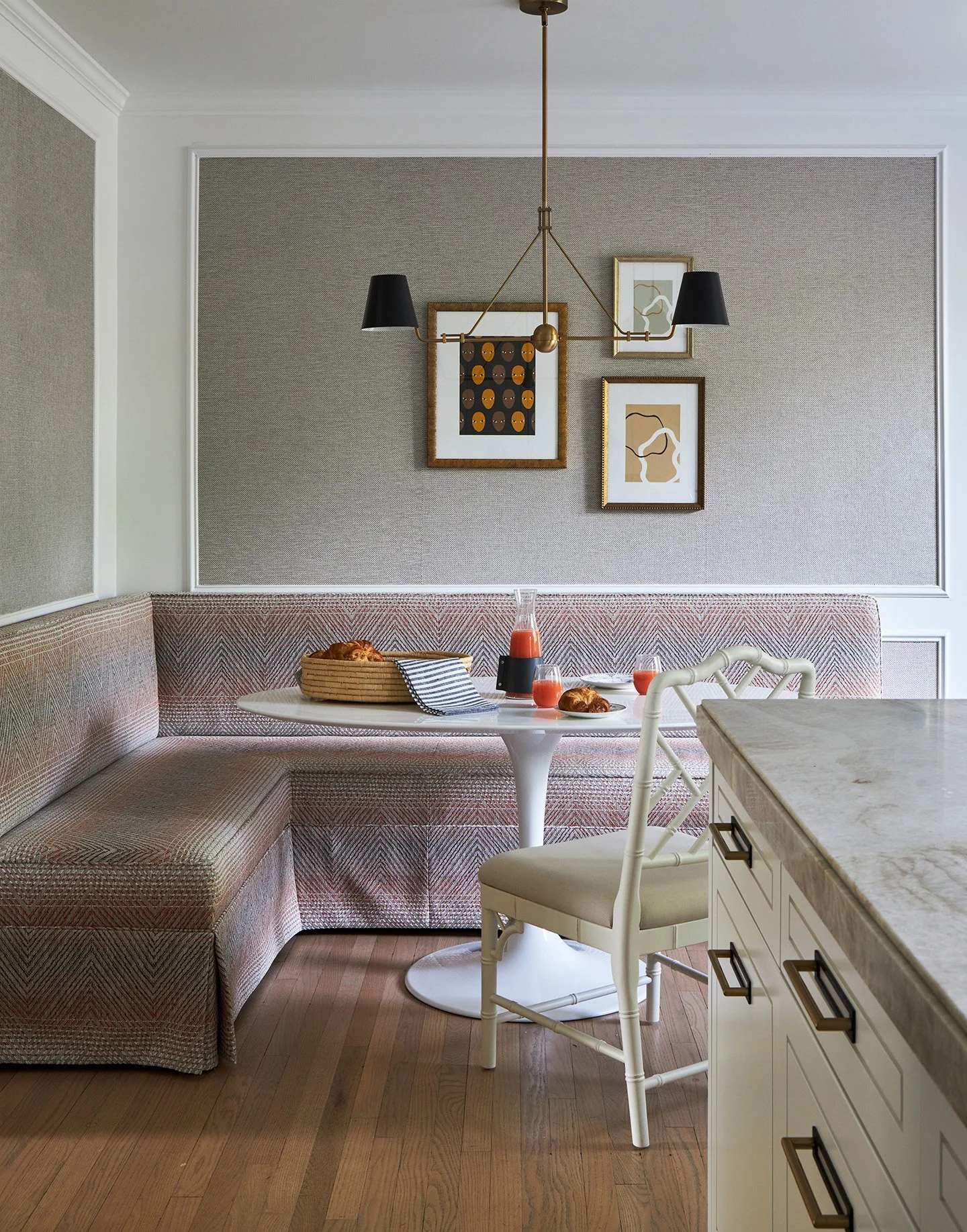 Breakfast nook with upholstered banquette, white tulip table, brass chandelier, and framed art gallery wall.