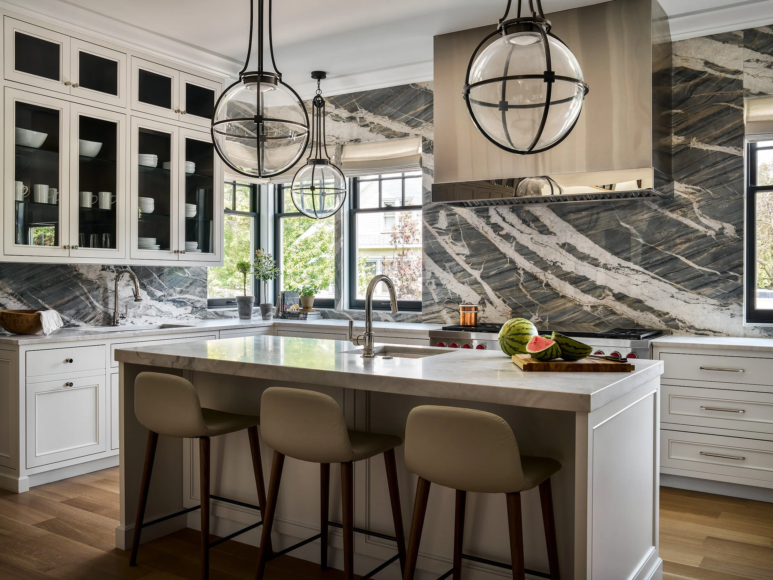 Modern kitchen featuring marble countertops, glass pendant lights, and a large island with bar seating.
