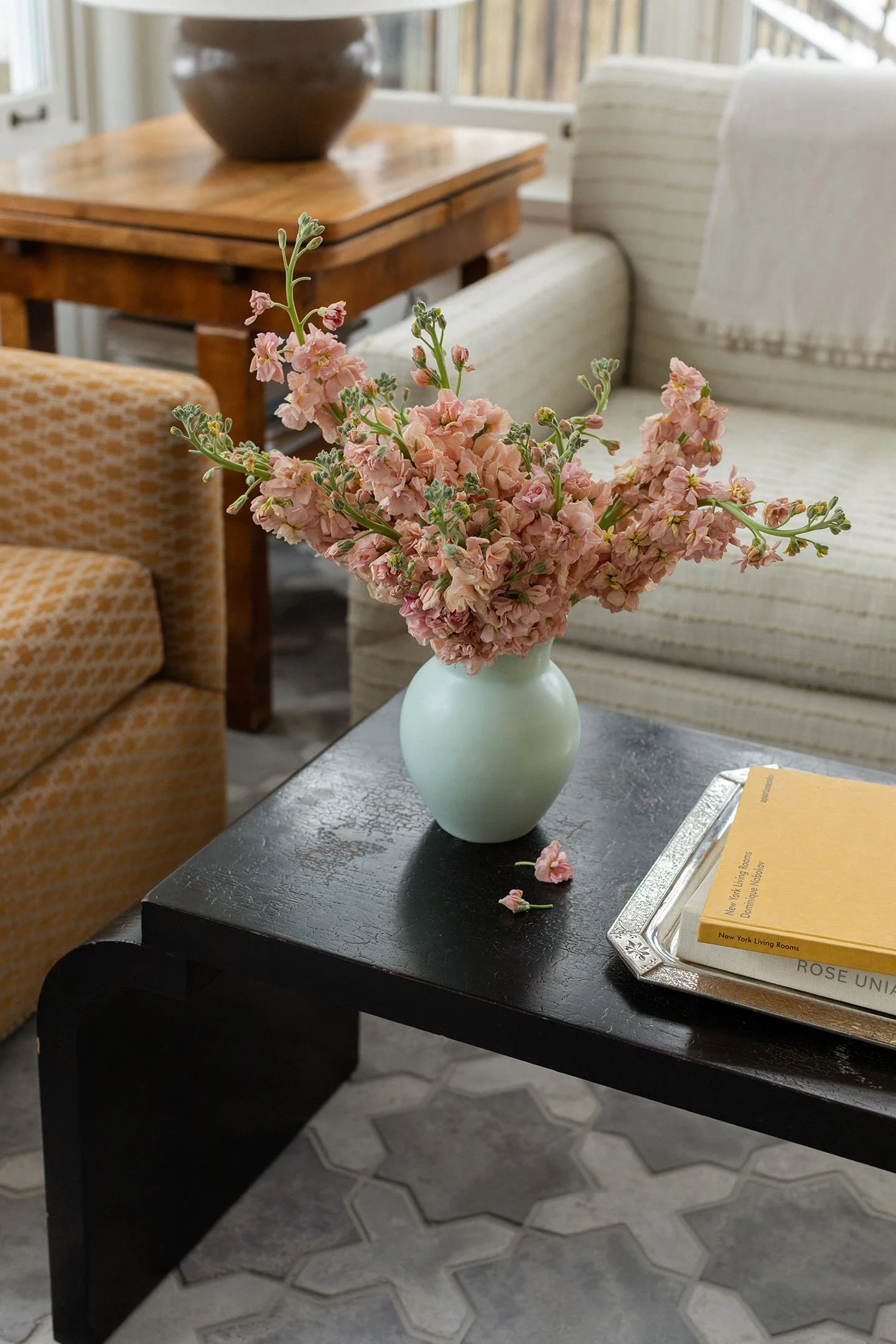 Pink floral arrangement in ceramic vase styled on black coffee table in a light-filled sitting room.
