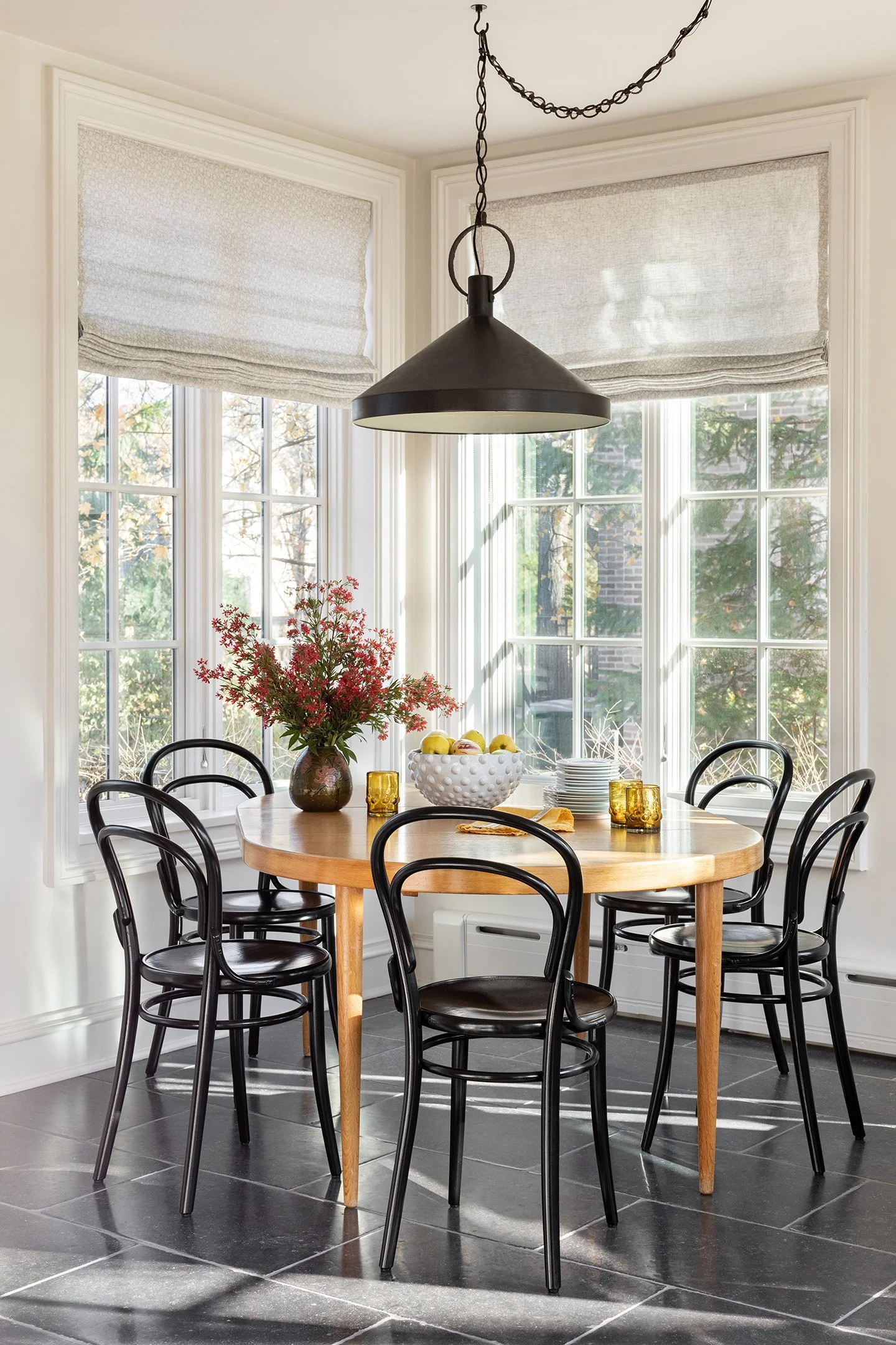 Sunlit breakfast nook with round wood table, black bentwood chairs, and oversized pendant light.