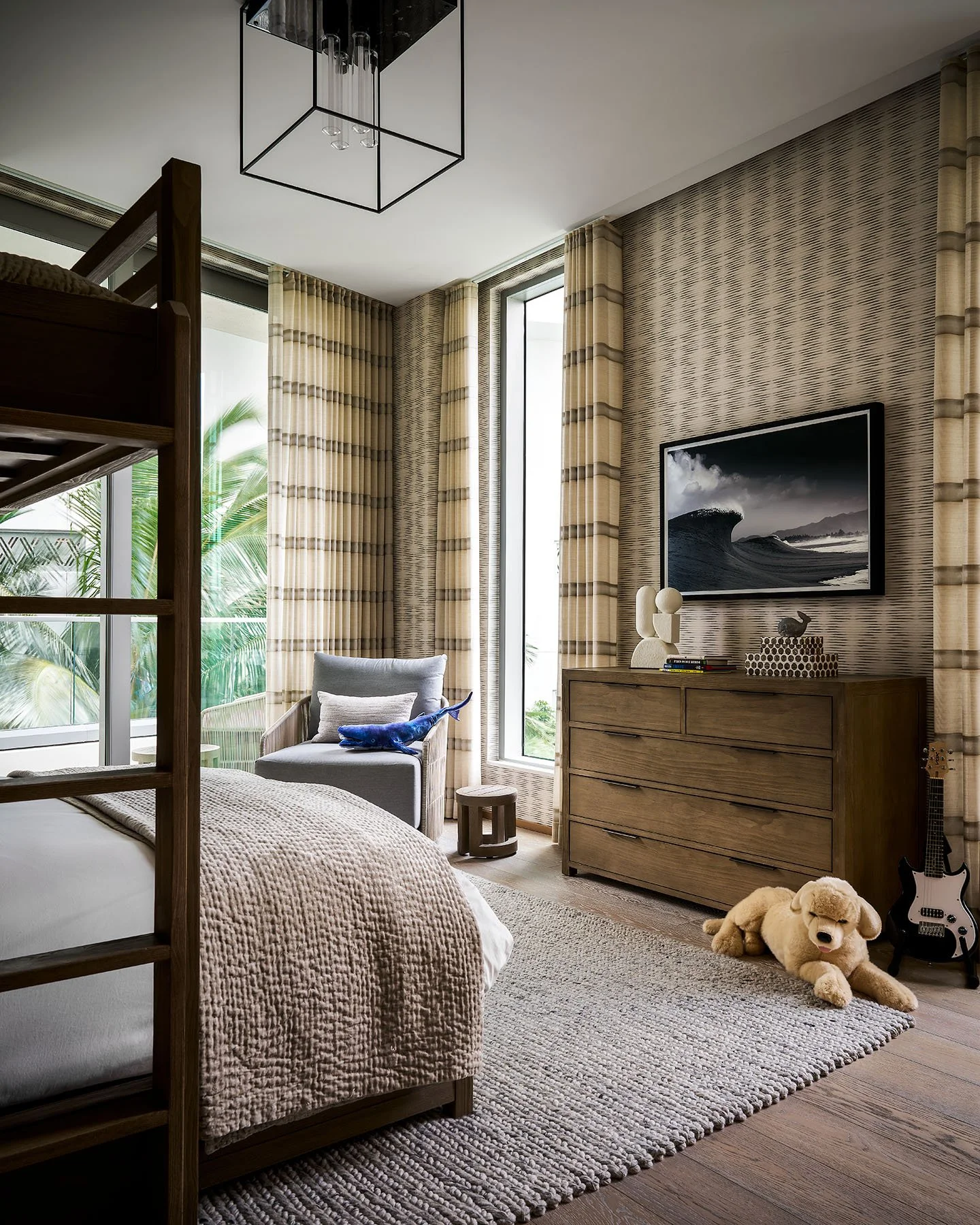 Modern boys bedroom with built-in bunk bed, textured wallpaper, wood dresser, and ocean view through large windows.
