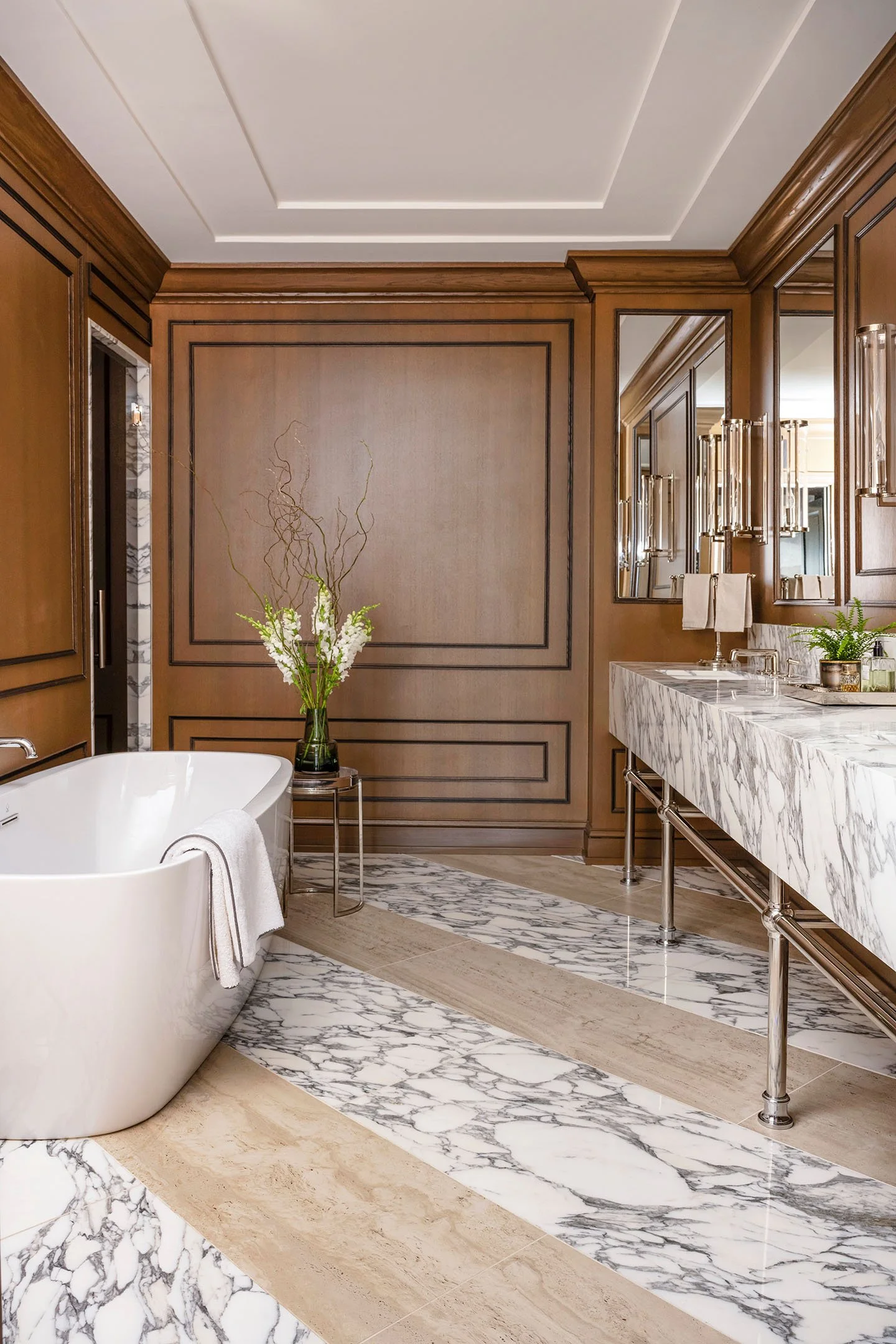 Luxury bathroom with freestanding soaking tub, marble flooring, custom wood paneling, and double vanity with polished nickel fixtures.