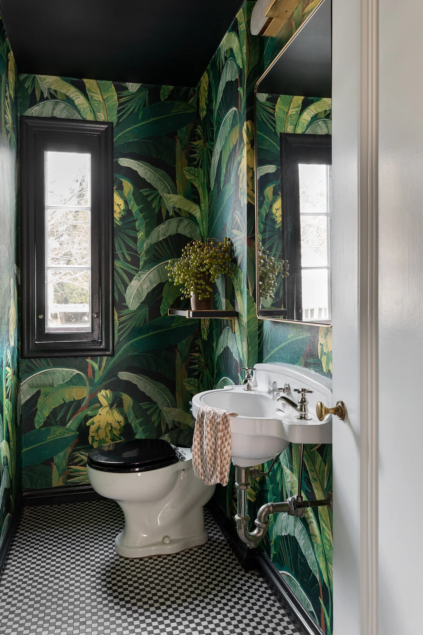 Powder room with bold tropical leaf wallpaper, pedestal sink, and black and white tile floor.