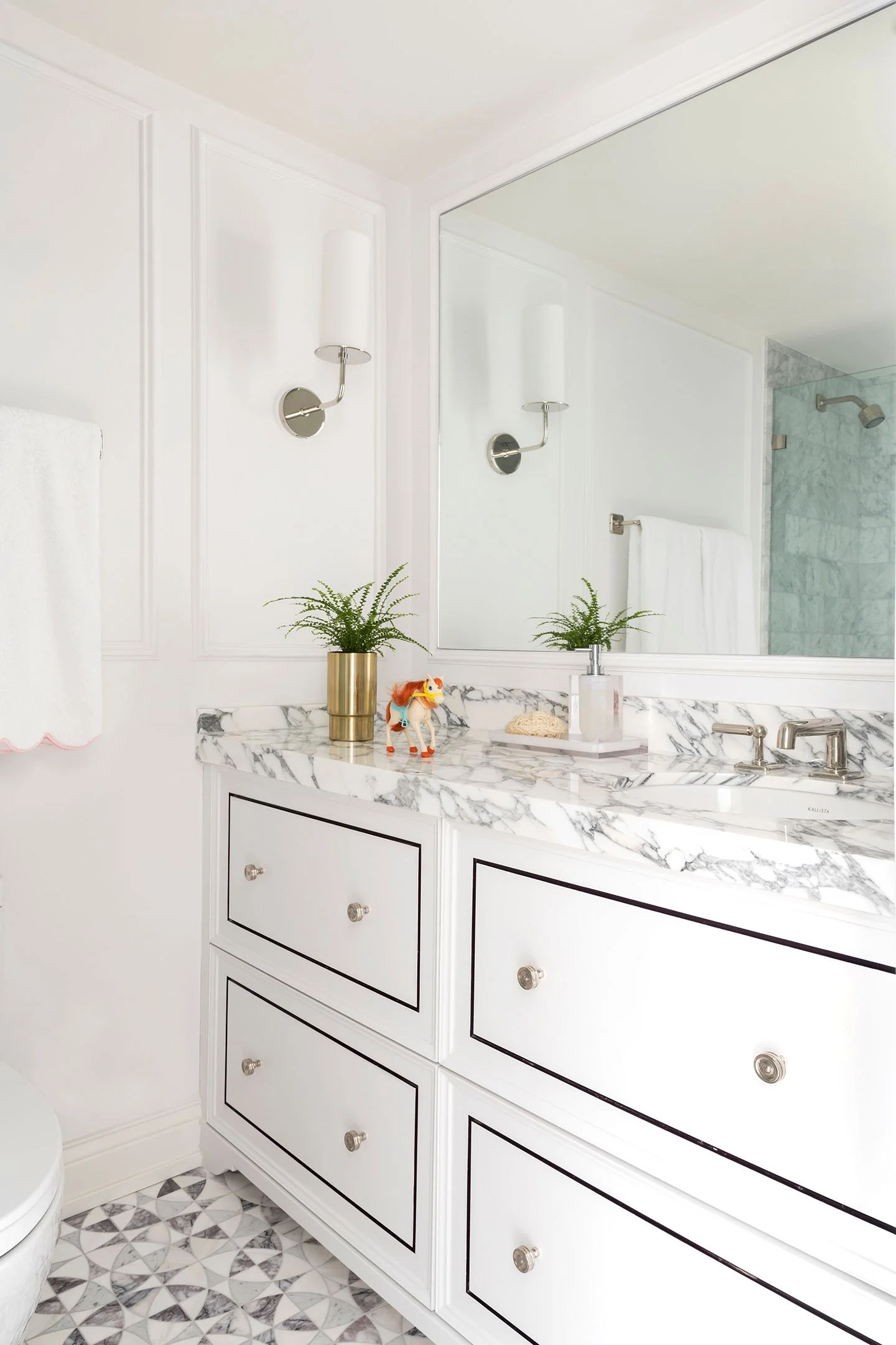 Bright kids bathroom with white vanity, marble countertop, polished nickel fixtures, and classic wall sconces.