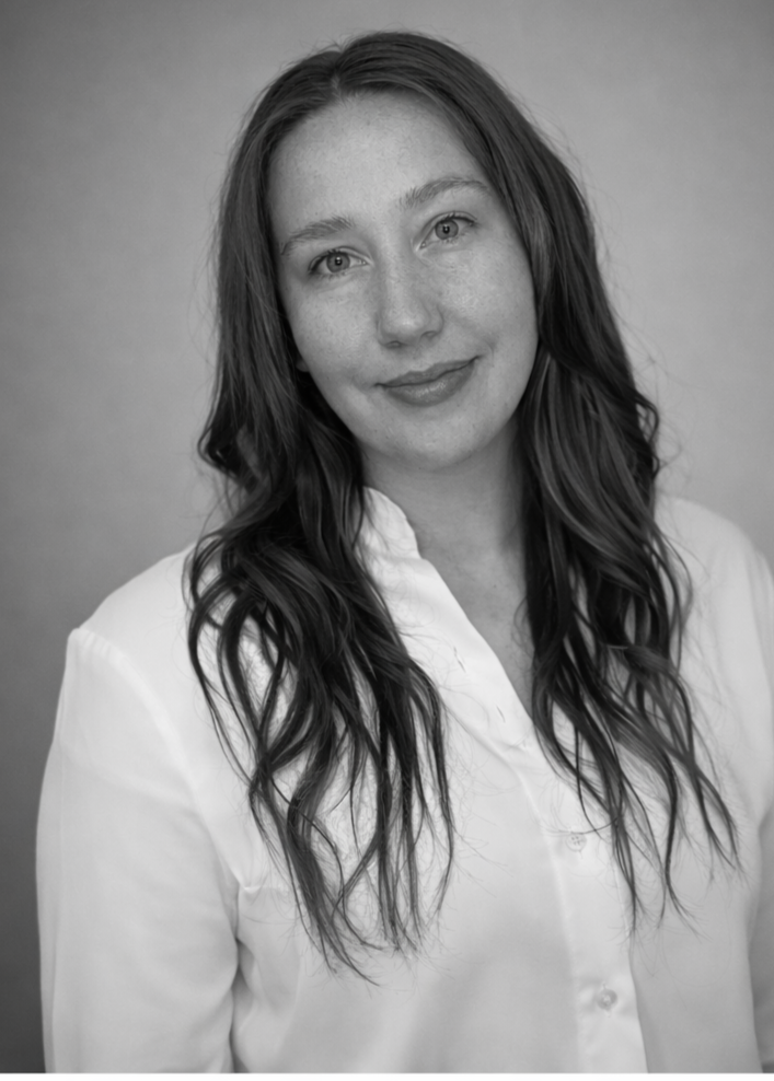 Black-and-white portrait of a woman with long wavy hair, wearing a white blouse, smiling softly at the camera.