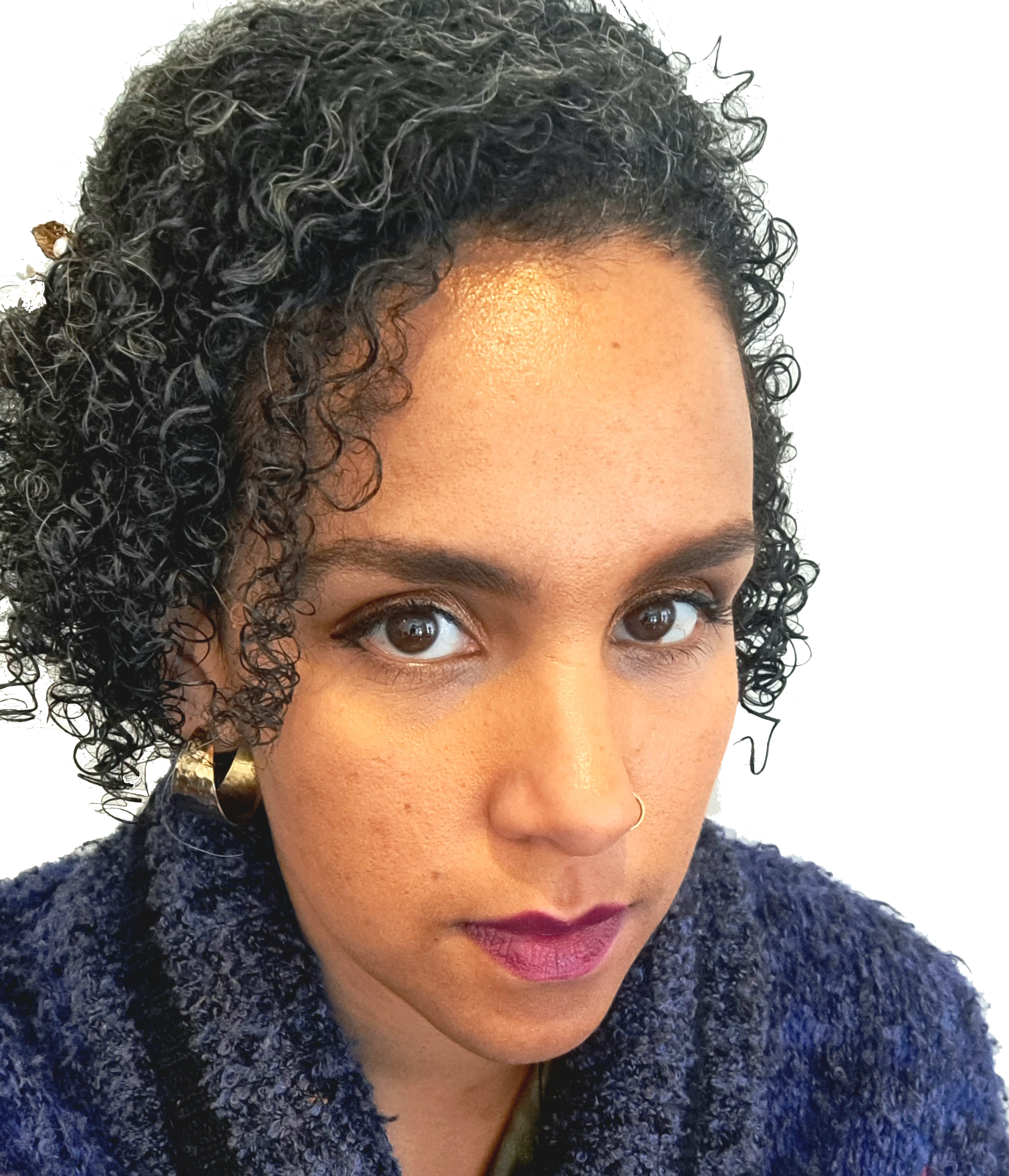 A woman with short, curly black hair, brown eyes, wearing gold hoop earrings, a nose ring, and a dark blue textured jacket, looking at the camera.