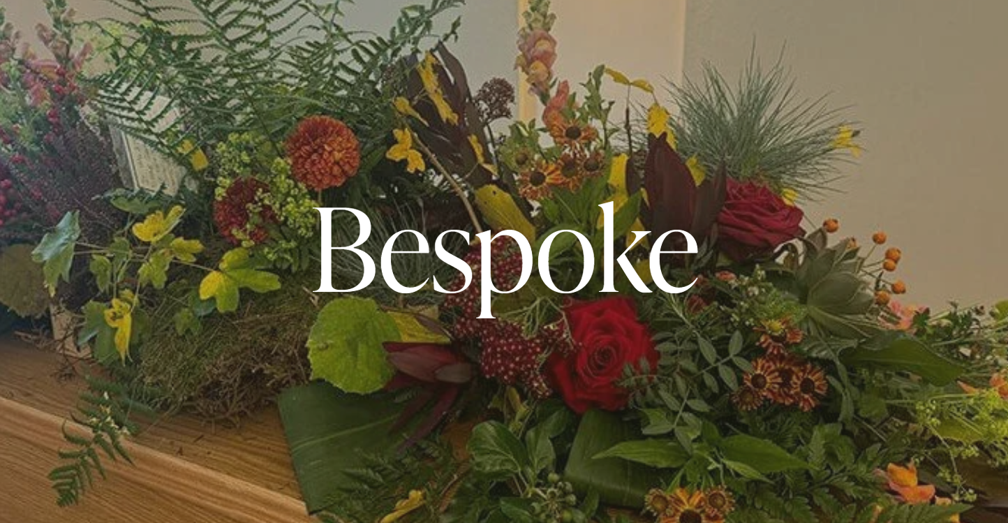 A floral arrangement with a mix of colorful flowers and greenery, resting on a wooden surface, with the word 'Bespoke' overlayed in white text.
