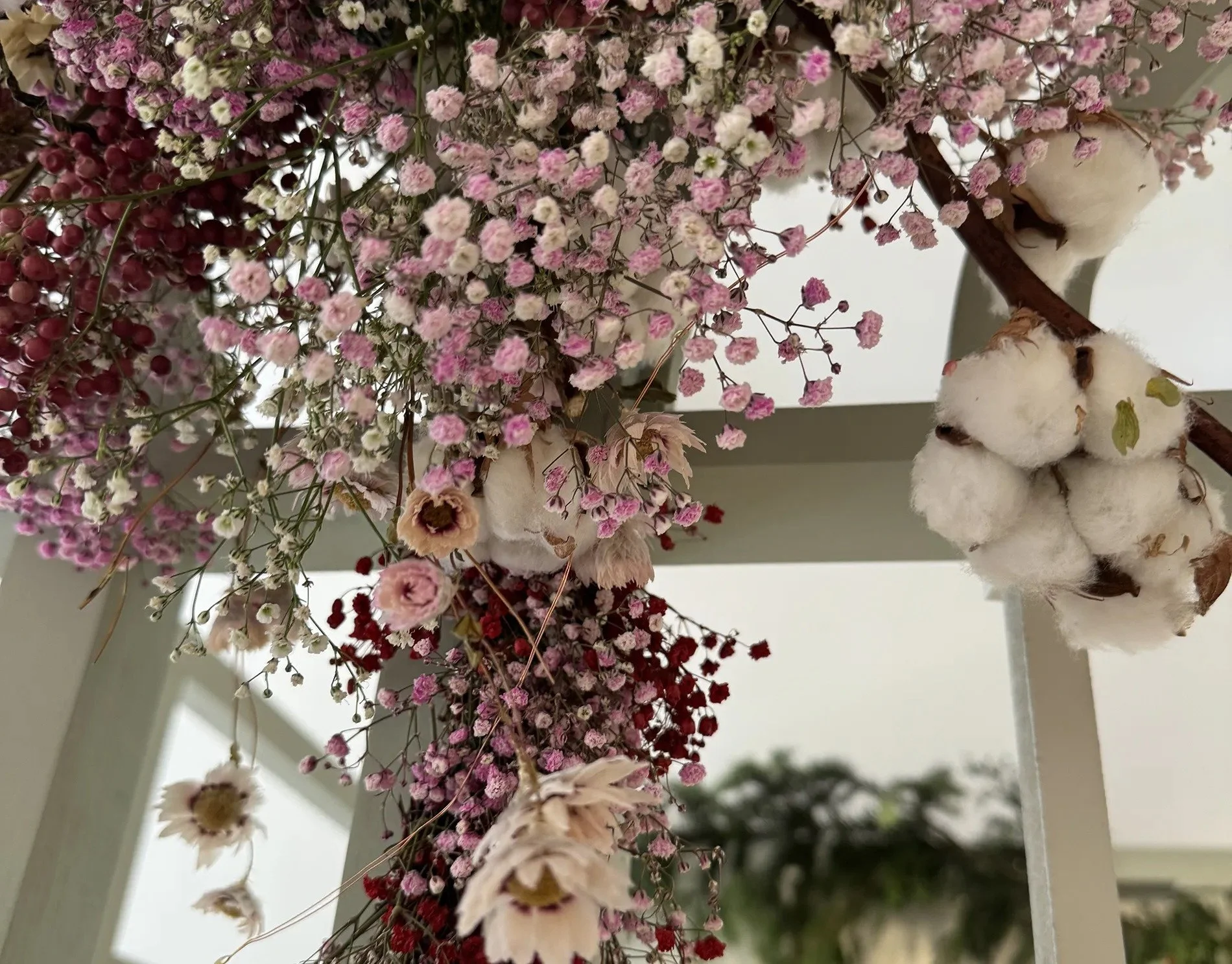 Close-up of dried pink, white, and red flowers and cotton branches hanging from a white metal frame.