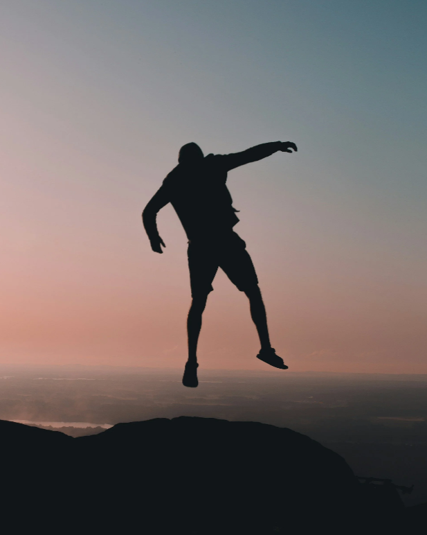 Silhouette of a person jumping in the air on a mountain during sunset.