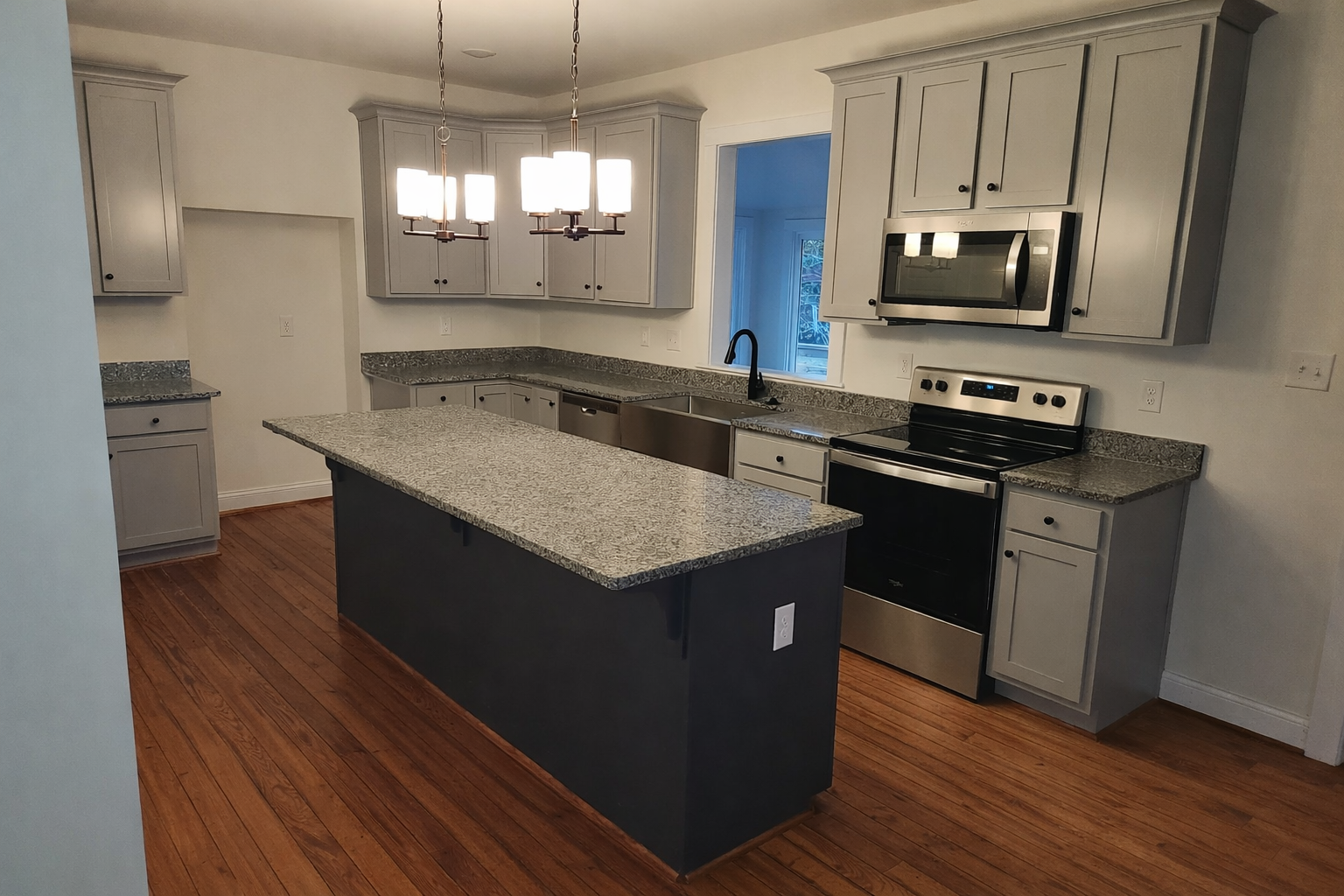 Modern kitchen with gray cabinets, granite countertops, a kitchen island, hardwood floors, stainless steel appliances, and a hanging light fixture.