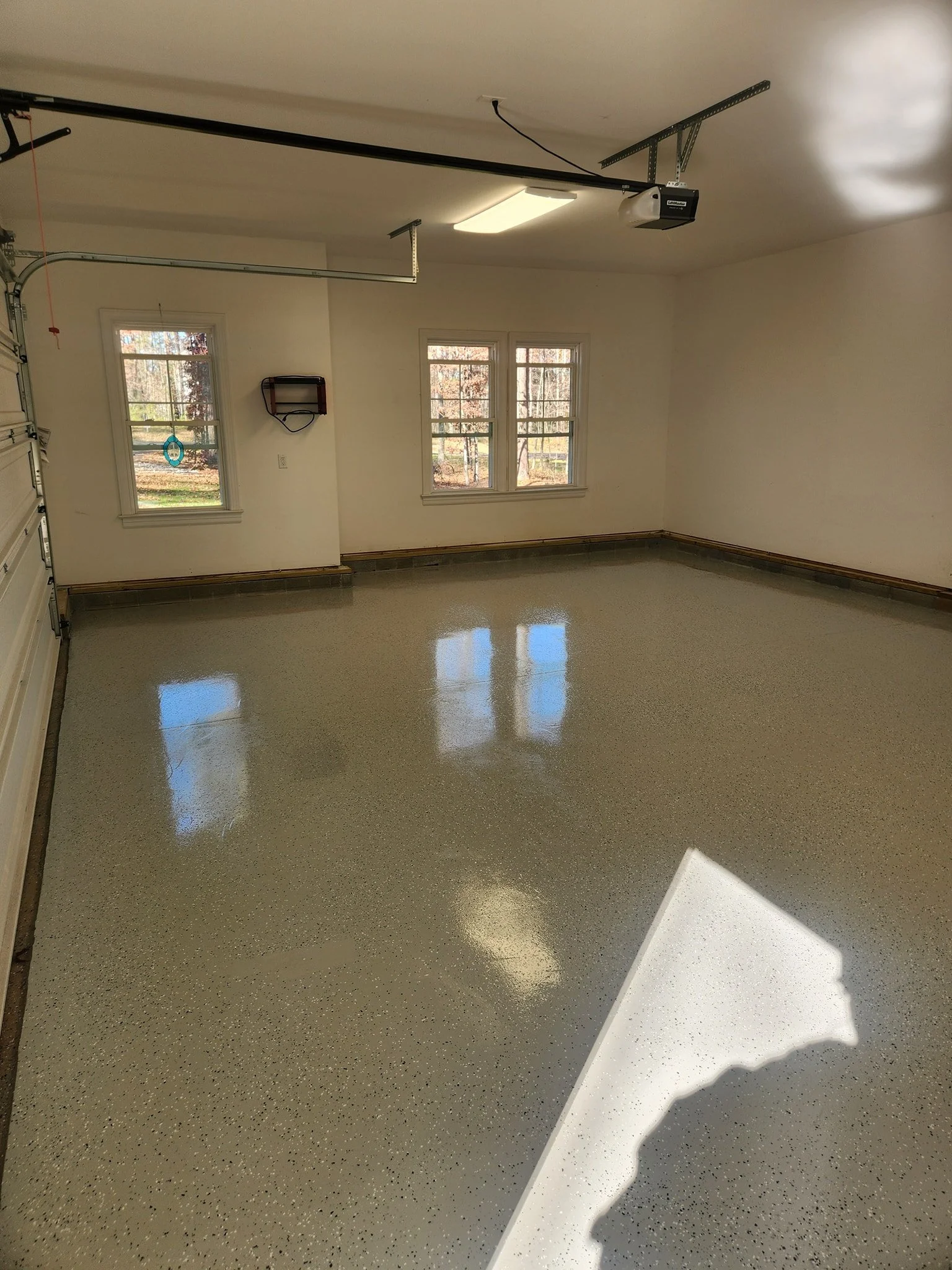 Empty garage with polished epoxy floor, three windows, and a garage door opener.